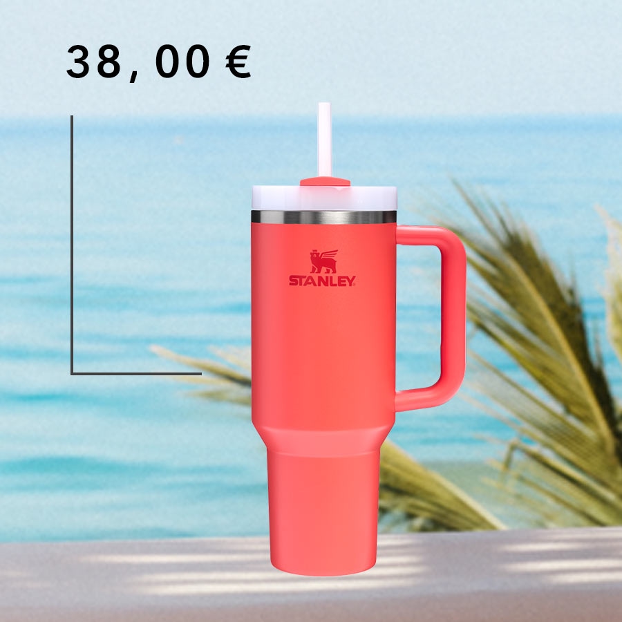 Hier ist ein korallfarbener Stanley Becher mit Henkel und Strohhalm, der vor einem Strand mit blauem Meer und Palmen für 38,00 € steht.