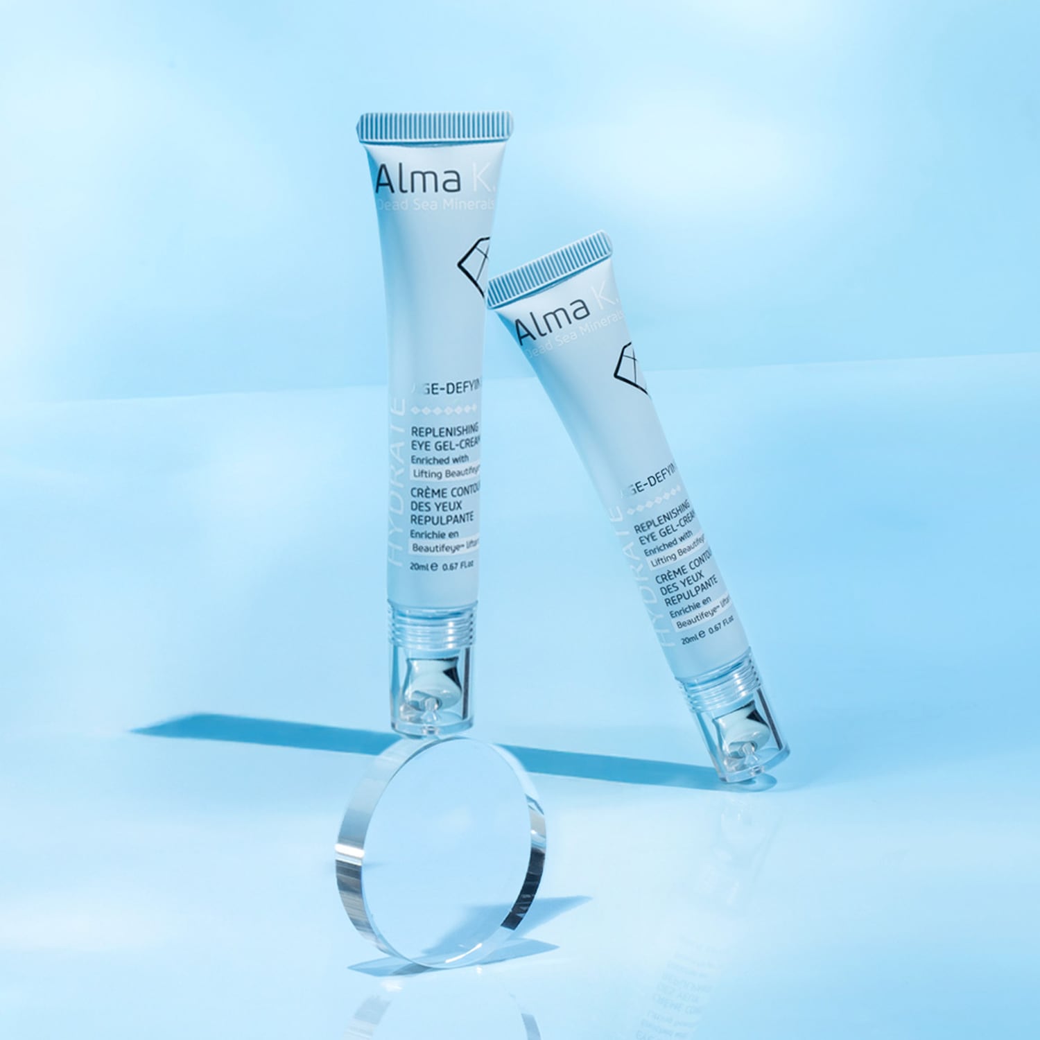 Ecco due tubetti di crema gel occhi rigenerante Alma K Dead Sea Minerals, presentati in un packaging azzurro chiaro e disposti su una superficie riflettente.