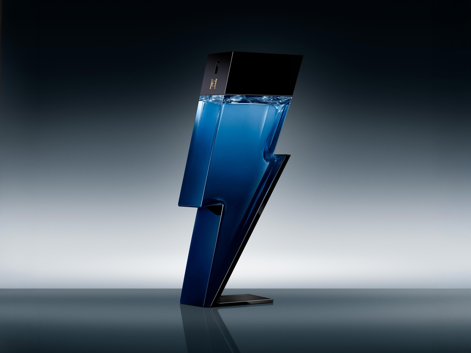 Un flacon de parfum Carolina Herrera Bad Boy, în formă de fulger albastru închis, cu un capac negru, este așezat pe o suprafață reflectorizantă, pe un fundal gri, cu o lumină puternică în spate.