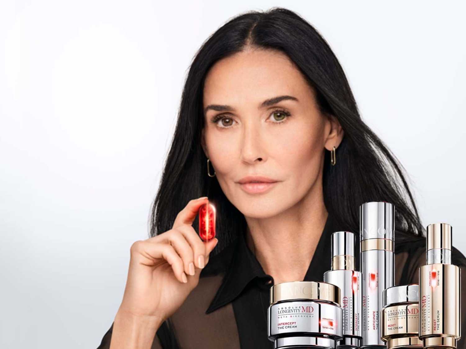 Demi Moore prezentuje linię produktów do pielęgnacji skóry Longevity MD, w tym kremy i serum w srebrnych opakowaniach z czerwonymi akcentami.