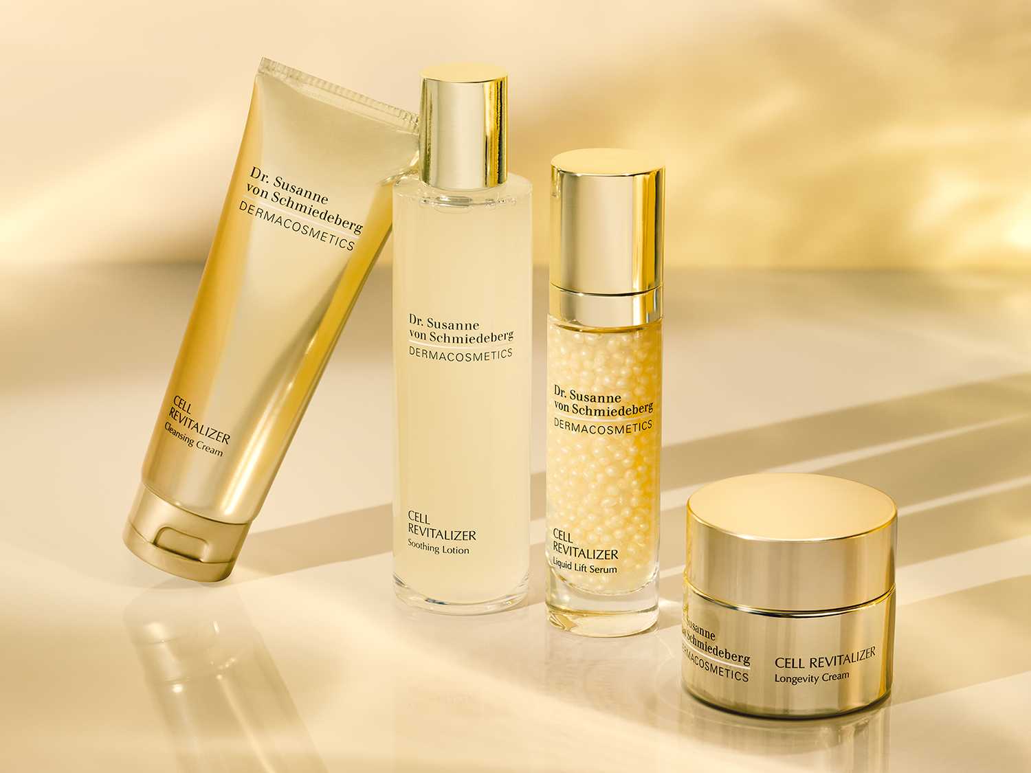 Cztery złote opakowania produktów do pielęgnacji skóry Dr. Susanne von Schmiedeberg DERMACOSMETICS z serii Cell Revitalizer, w tym krem oczyszczający, tonik łagodzący, serum liftingujące i krem na długowieczność.