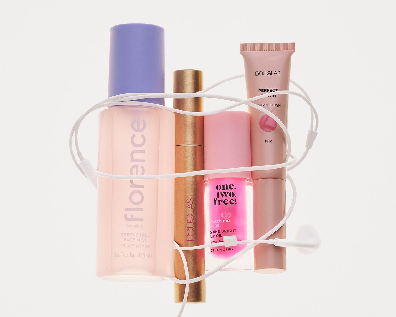 Na bílém pozadí jsou uspořádány čtyři kosmetické produkty: pleťová mlha Florence by Mills Zero Chill, řasenka Douglas, lesk na rty One.Two.Free! Shine Bright Lip Oil a tvářenka Douglas Perfect Focus Early Blush, vše propletené bílými sluchátky.