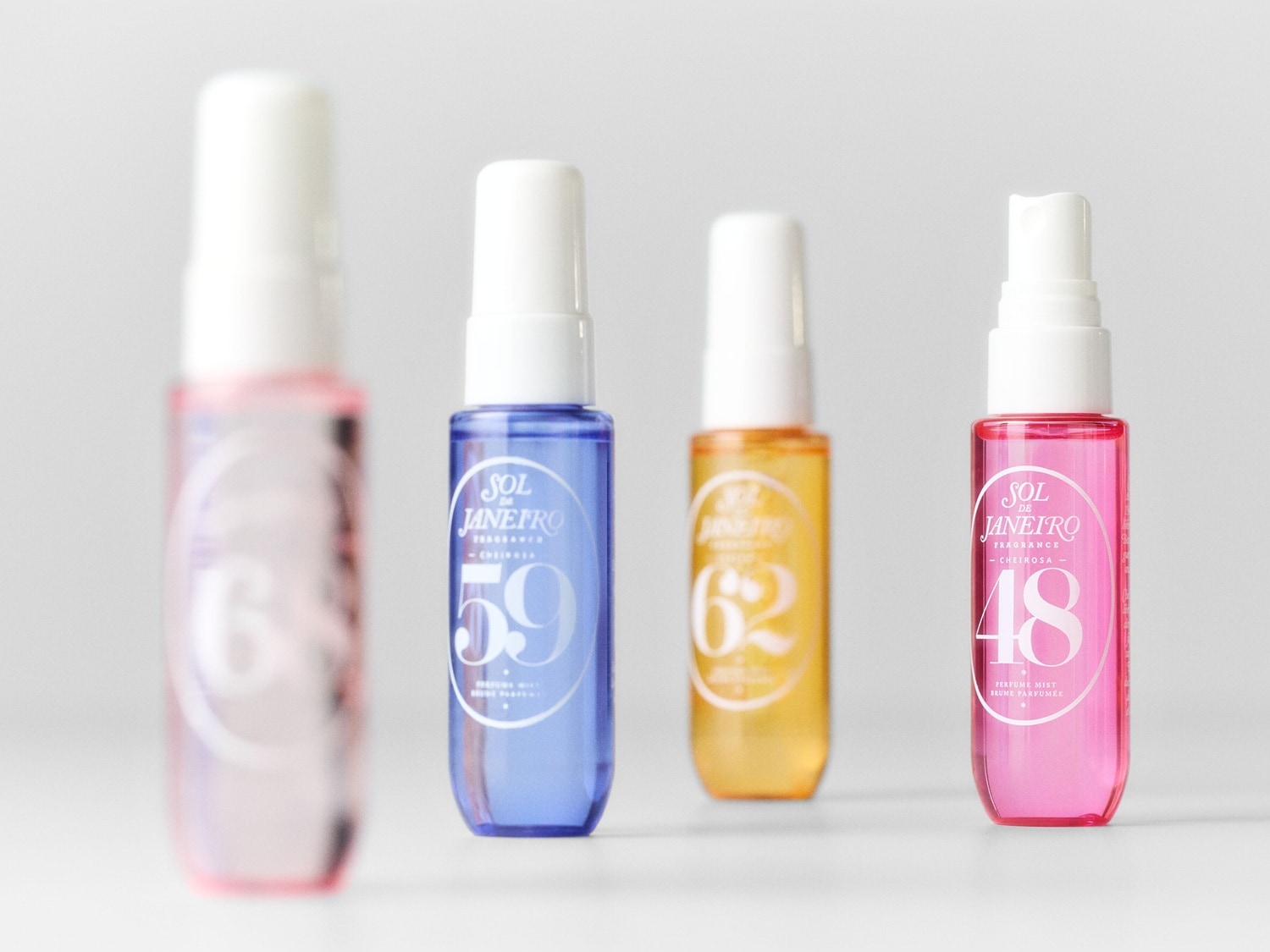 Découvrez quatre flacons de parfum Sol de Janeiro aux couleurs vives : rose clair, bleu, jaune et rose vif, chacun avec un bouchon blanc et un numéro distinctif.