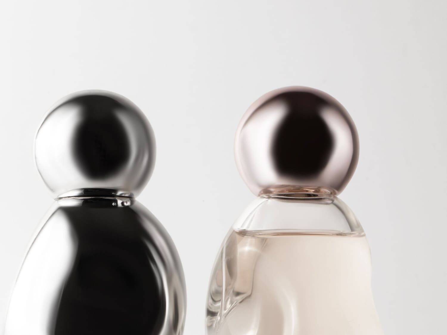Nahaufnahme von zwei Parfümflaschen, eine in glänzendem Silber und die andere in durchsichtigem Glas mit einem roségoldenen Verschluss.