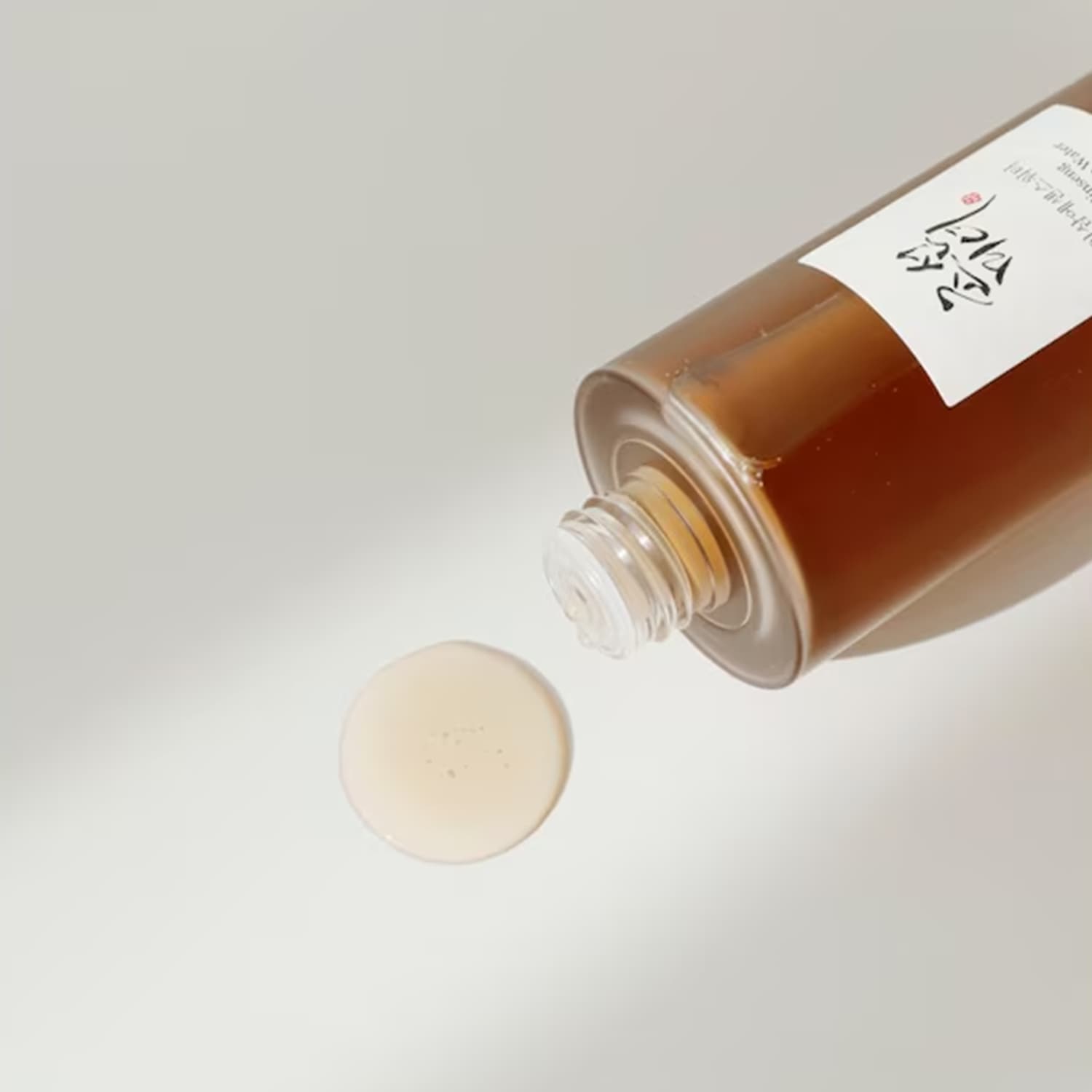 Flacone ambrato di tonico all'ginseng che versa una goccia di prodotto, ideale per idratare e rivitalizzare la pelle.