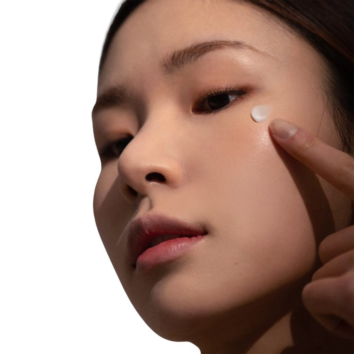 Primo piano di una donna che applica una crema bianca sotto l'occhio con un dito, per idratare e illuminare la zona.