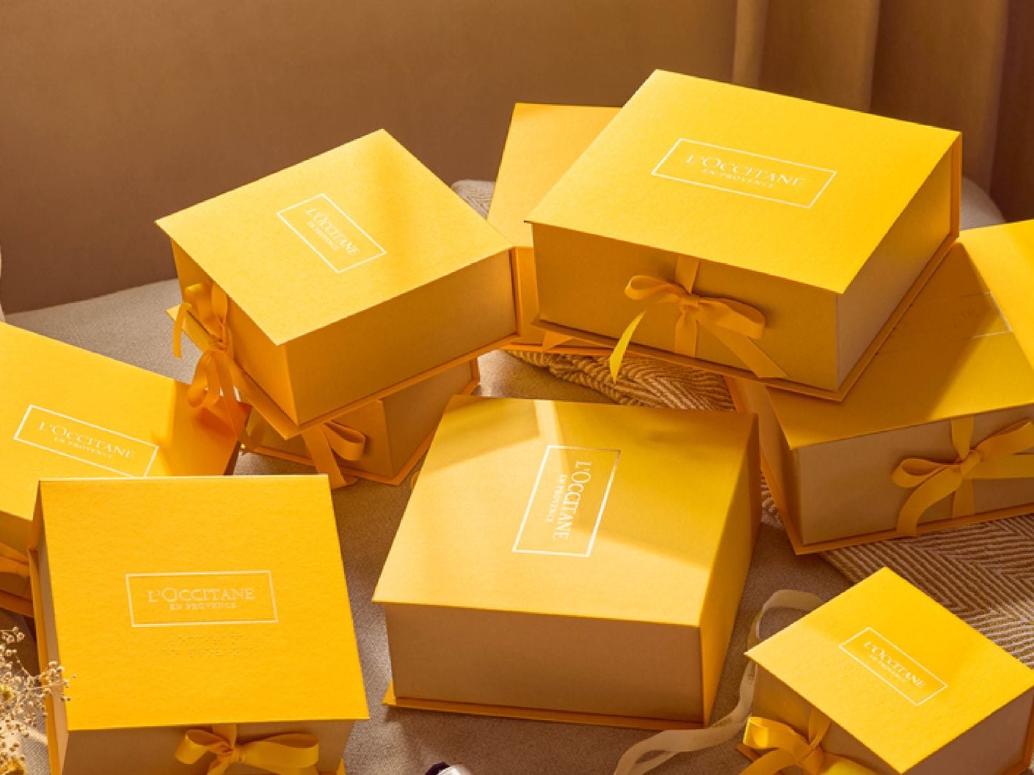 Mehrere gelbe Geschenkboxen von L'OCCITANE mit gelben Schleifen liegen neben- und übereinander.