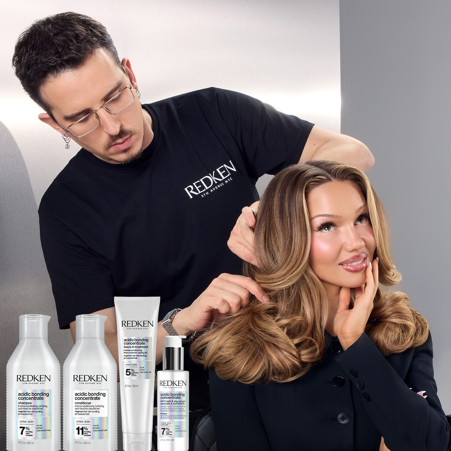 Shirin David sitzt auf einem Stuhl mit einem Friseur hinter ihr und weißen Produkten von Redken unten links in der Ecke.