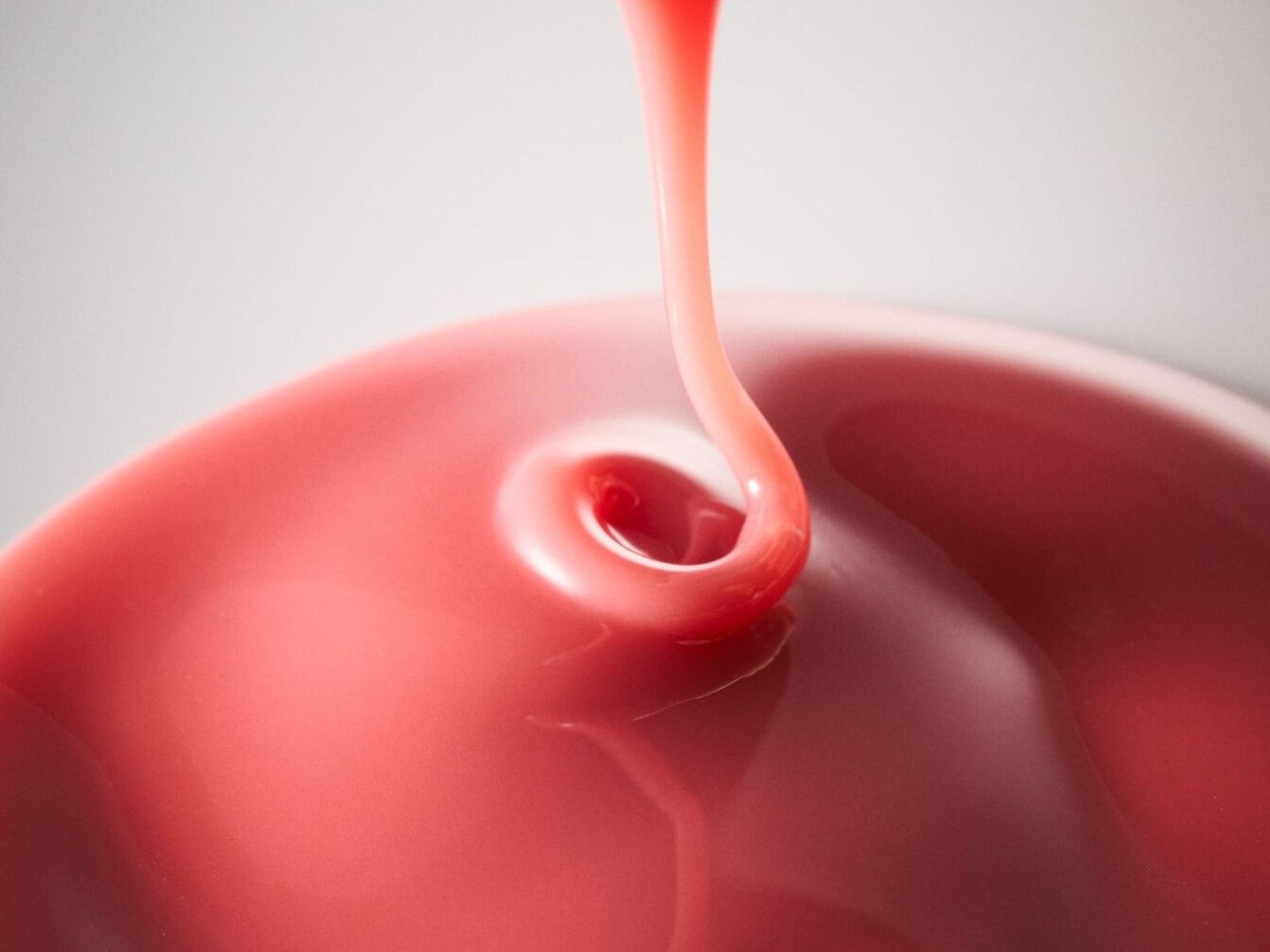 Ein glänzender, rosafarbener Lipgloss oder eine Flüssigkeit wird in eine Schale gegossen und bildet eine Wirbelform, die die luxuriöse Textur und Farbe des Produkts hervorhebt.
