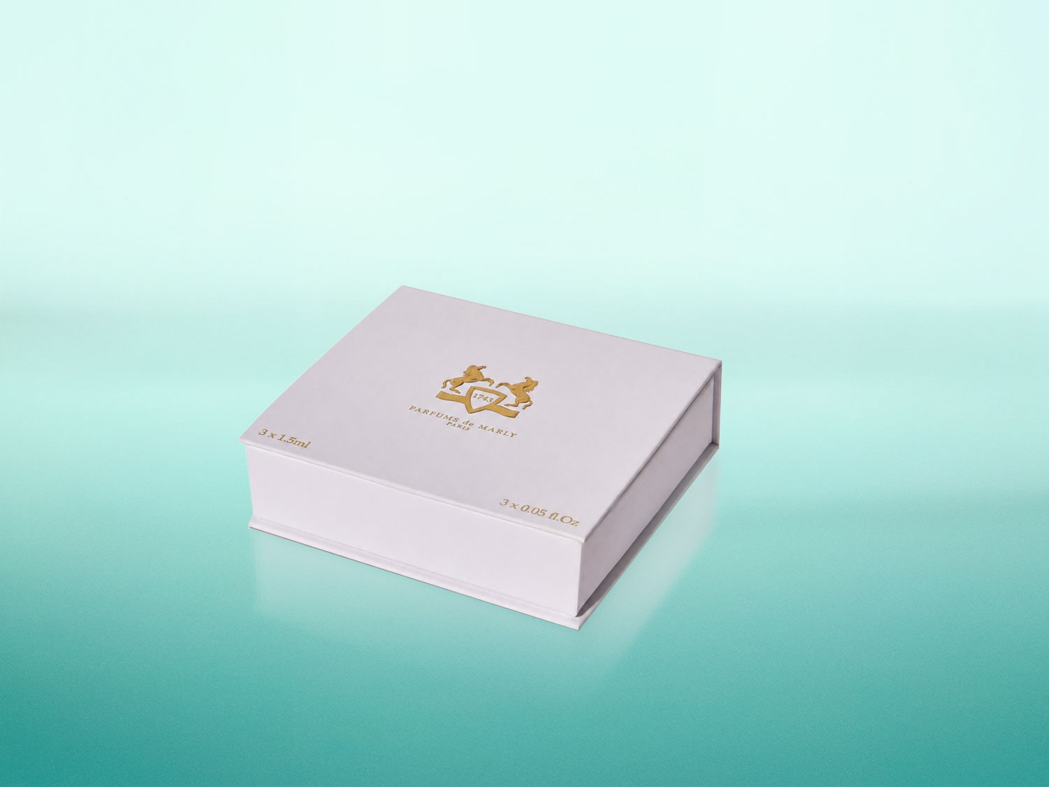 Eine weiße Schachtel mit goldenem Logo und der Aufschrift "PARFUMS de MARLY PARIS" sowie "3 x 1.5ml" und "3 x 0.05 fl.Oz" auf einem türkisfarbenen Hintergrund.