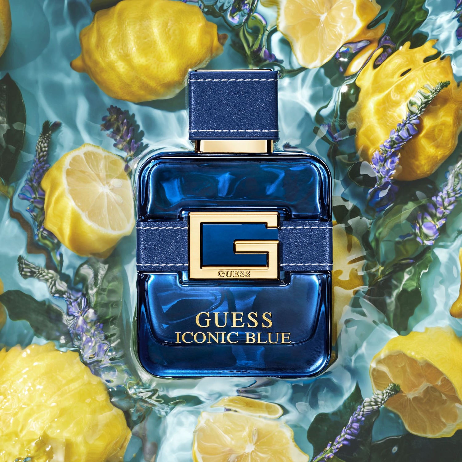 Il profumo Guess Iconic Blue è presentato in una bottiglia blu scuro con un tappo in pelle blu e dettagli dorati, immerso in acqua con limoni freschi e fiori di lavanda.