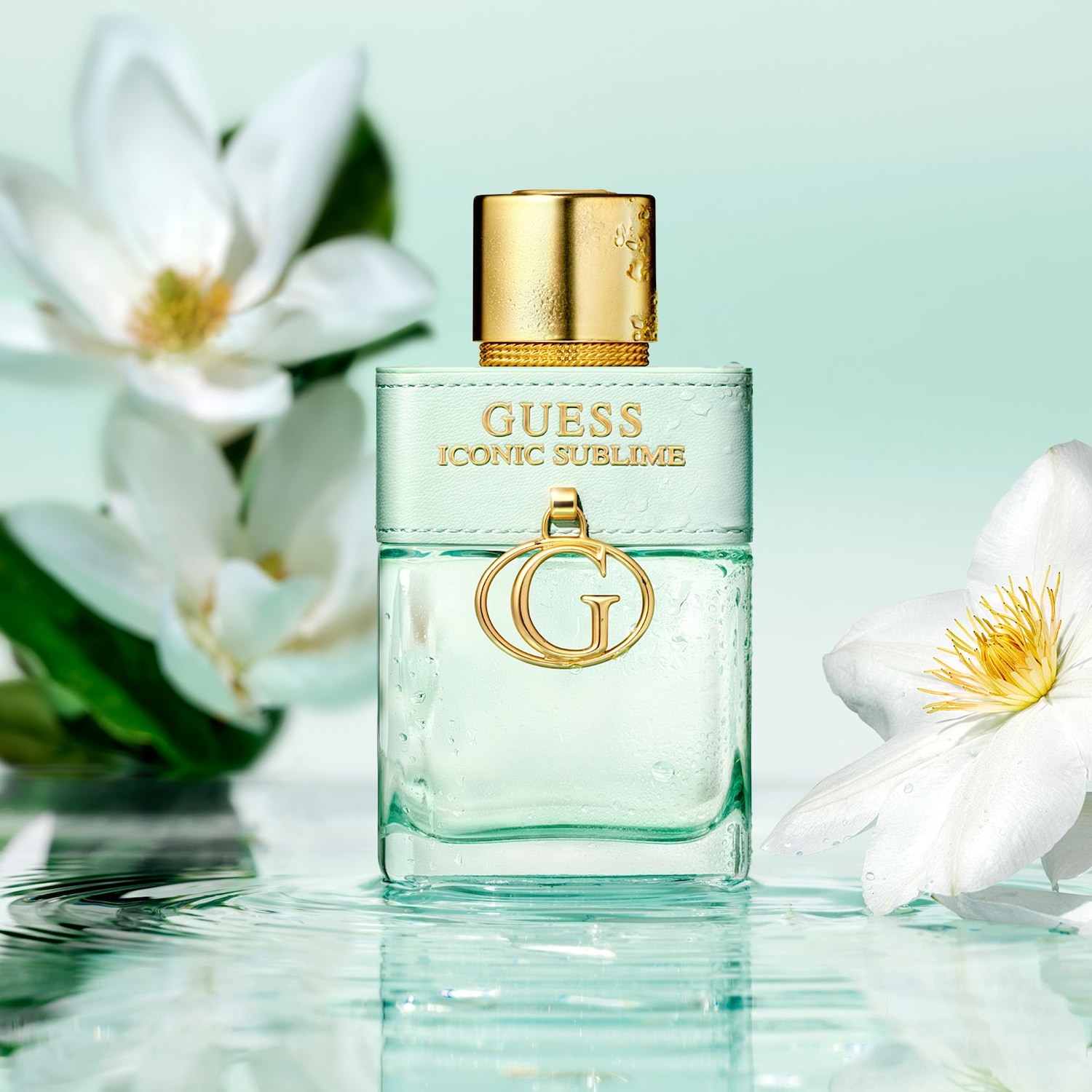 Il profumo Guess Iconic Sublime è presentato in una bottiglia rettangolare di vetro verde acqua con un tappo dorato e un'etichetta in pelle verde acqua, circondato da fiori bianchi e goccioline d'acqua.