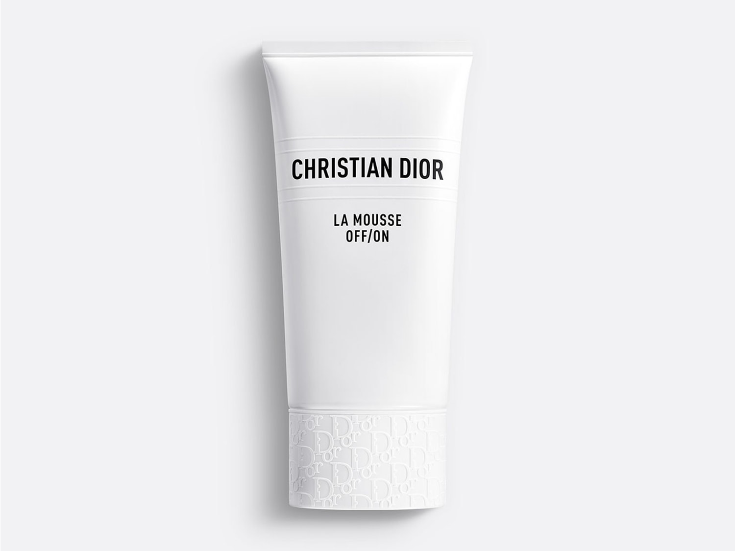 De Christian Dior La Mousse OFF/ON gezichtsreiniger in een witte tube met zwarte letters en een subtiel Dior-logo patroon aan de onderkant, staat klaar om je huid te reinigen.