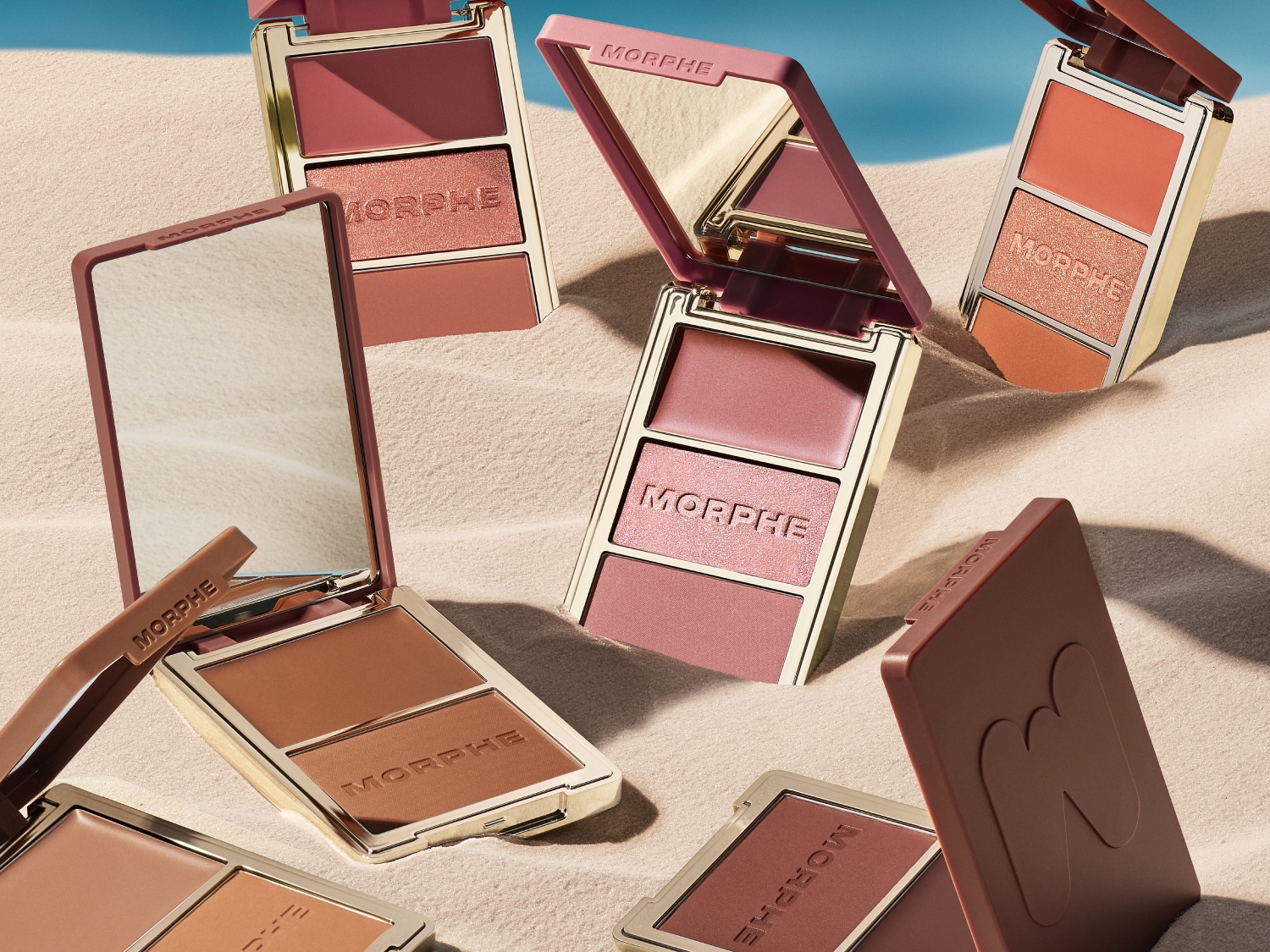 Découvrez les palettes de maquillage Morphe, avec des fards à paupières et des blushs aux teintes chaudes et naturelles, présentées sur un fond de sable clair.