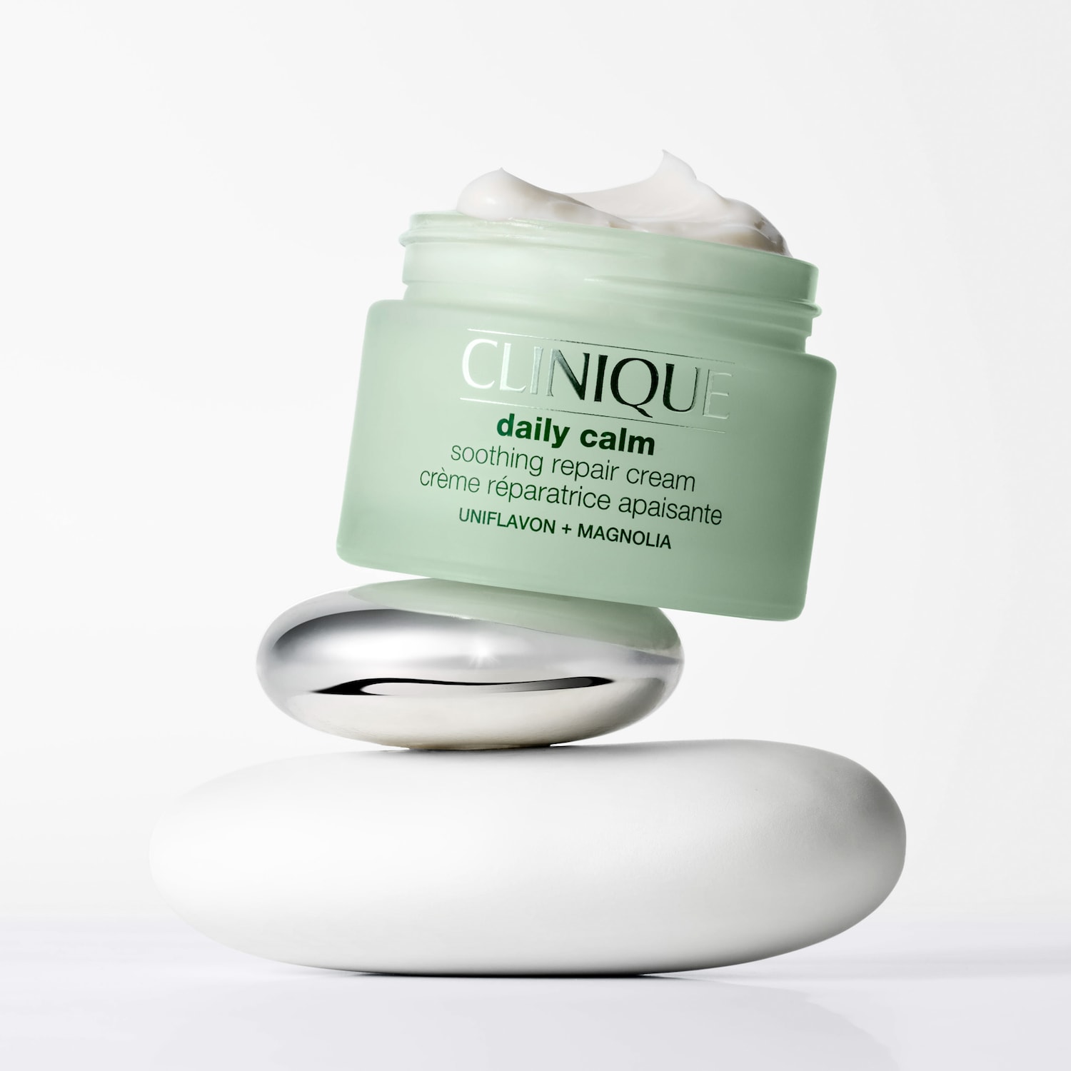 Ein geöffneter Tiegel Clinique Daily Calm Moisturizer Cream balanciert auf zwei flachen gestapelten Steinen.