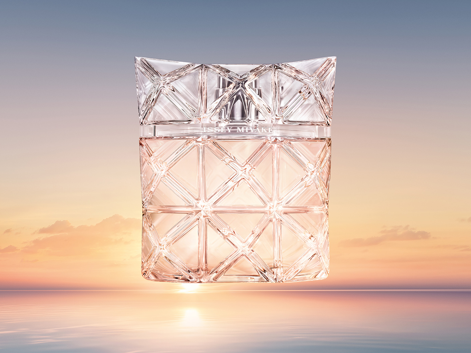 Der Issey Miyake "Lumière d'Issey" Duft präsentiert sich in einem transparenten, geometrisch geschliffenen Flakon mit zartroséfarbener Flüssigkeit vor einem Sonnenaufgang über dem Meer.