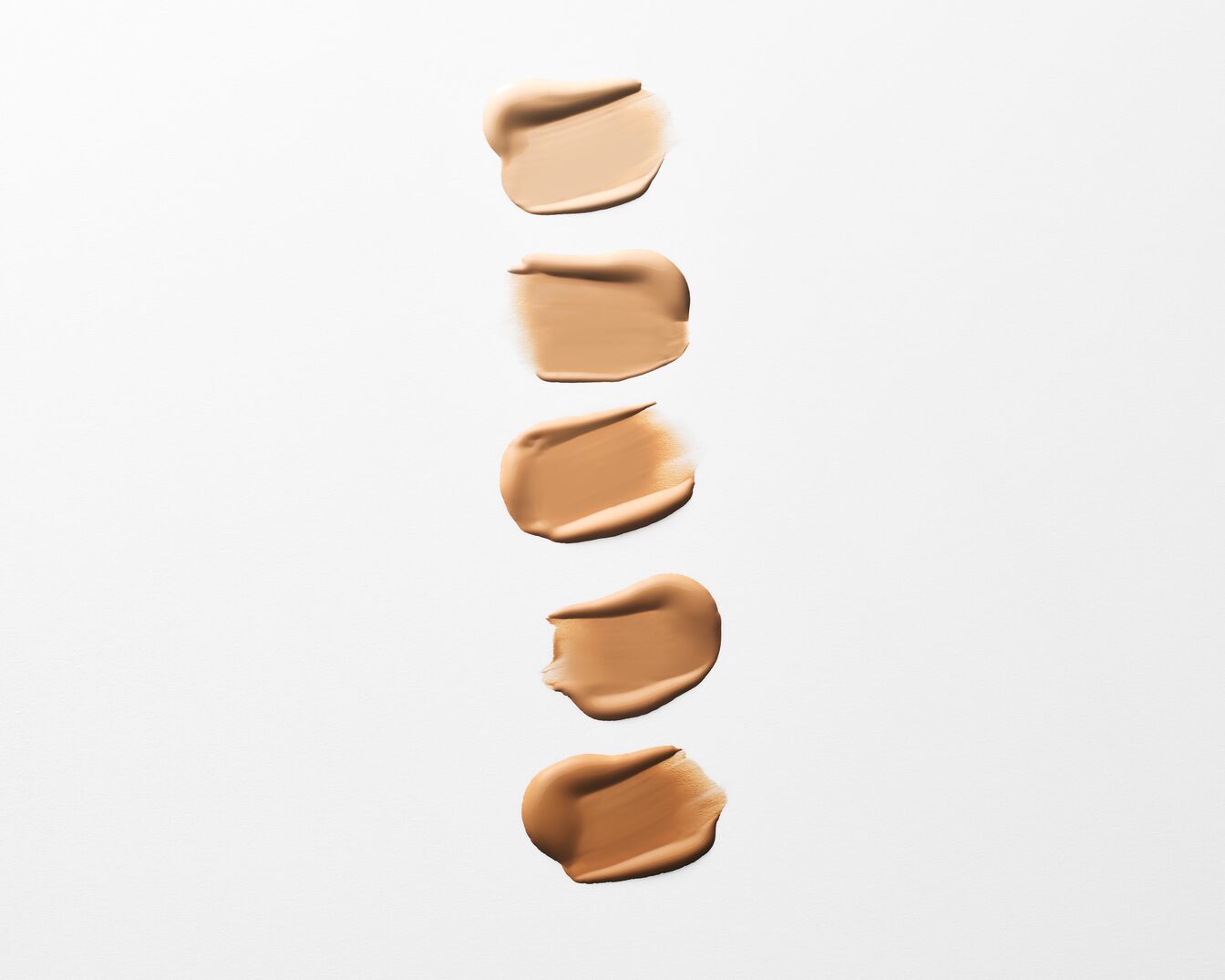 Fünf verschiedene Farbtöne von flüssiger Foundation sind in Swatches auf einem weißen Hintergrund zu sehen, die von hellbeige bis zu einem mittleren Braunton reichen und die Vielfalt der verfügbaren Nuancen zeigen.