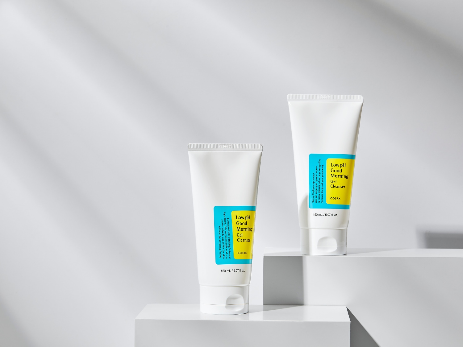 Dos tubos blancos de COSRX Low pH Good Morning Gel Cleanser, cada uno con una etiqueta amarilla y azul que describe el producto como un limpiador suave y refrescante para la piel.