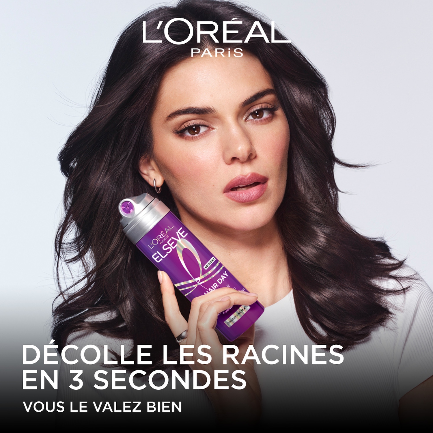 Une femme aux cheveux bruns tient une bombe de laque violette L'Oréal Elseve Hair Day, avec le texte "Décolle les racines en 3 secondes" et "Vous le valez bien".