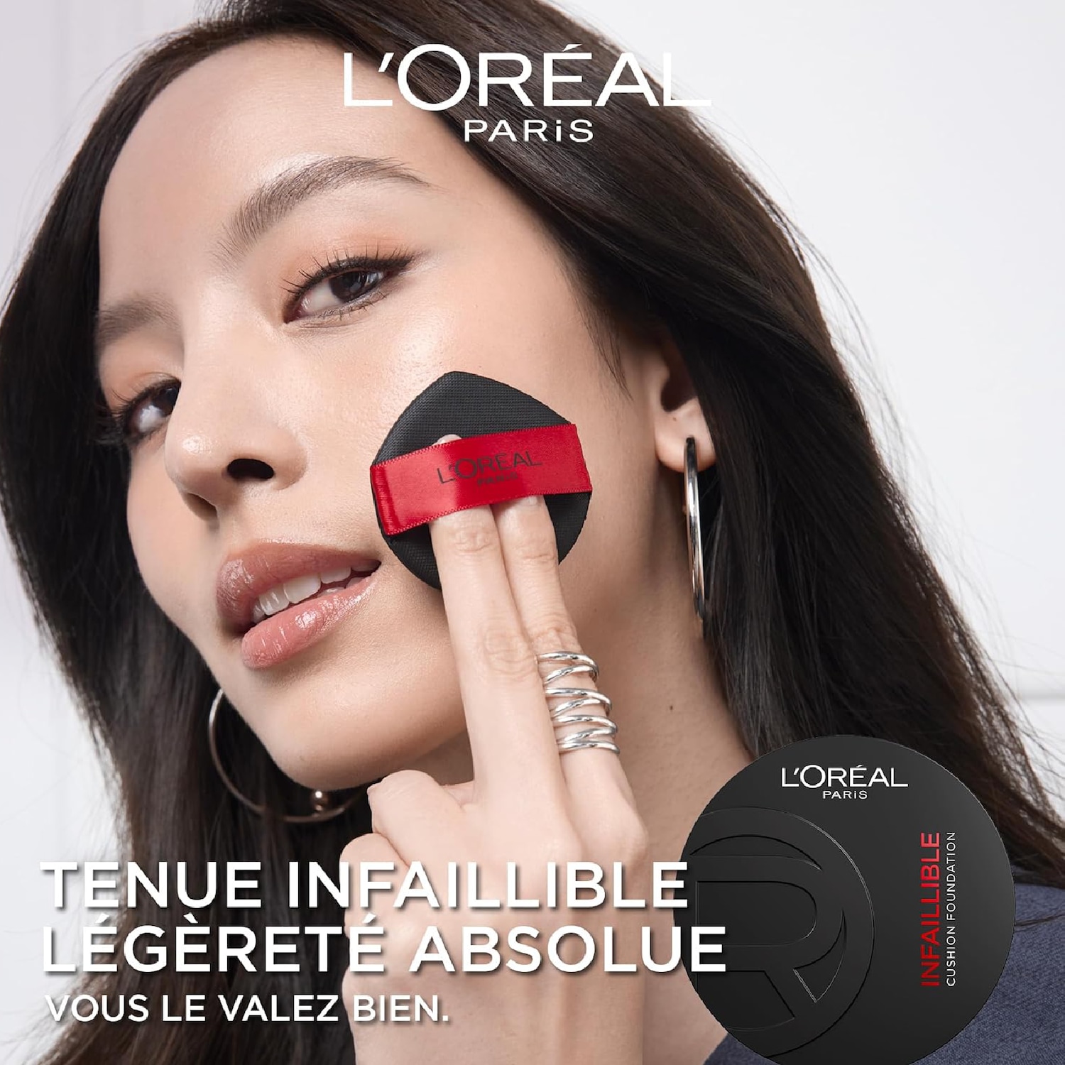 Une femme applique le fond de teint coussin Infaillible de L'Oréal Paris avec une éponge noire et rouge, affichant un teint impeccable et une tenue infaillible.