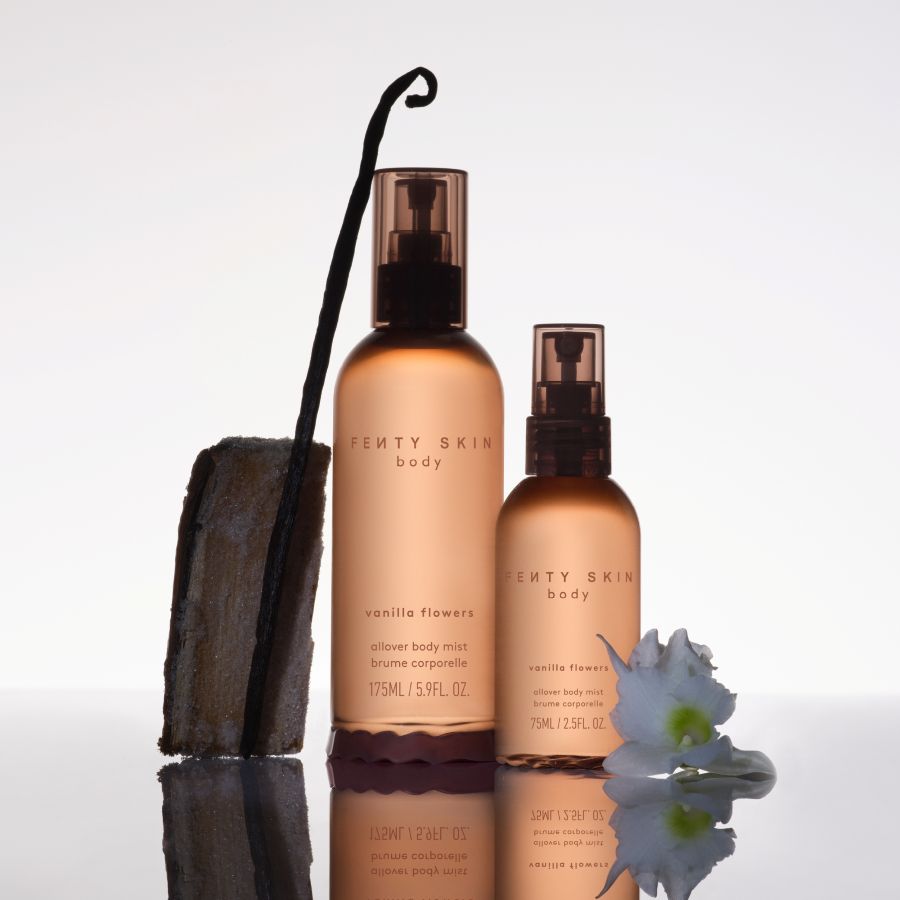 Deux flacons de brume corporelle Fenty Skin Body "Vanilla Flowers" sont présentés, l'un de 175 ml et l'autre de 75 ml, accompagnés d'une gousse de vanille et d'une fleur blanche.