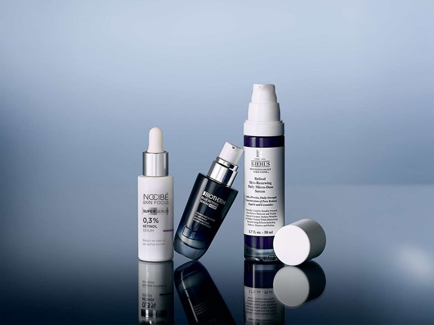 Trois sérums au rétinol sont présentés sur un fond bleu-gris, avec le sérum Nocibé Skin Focus 0,3% Rétinol, le sérum Biotherm Blue Retinol et le sérum Kiehl's Retinol Skin-Renewing Daily Micro-Dose.
