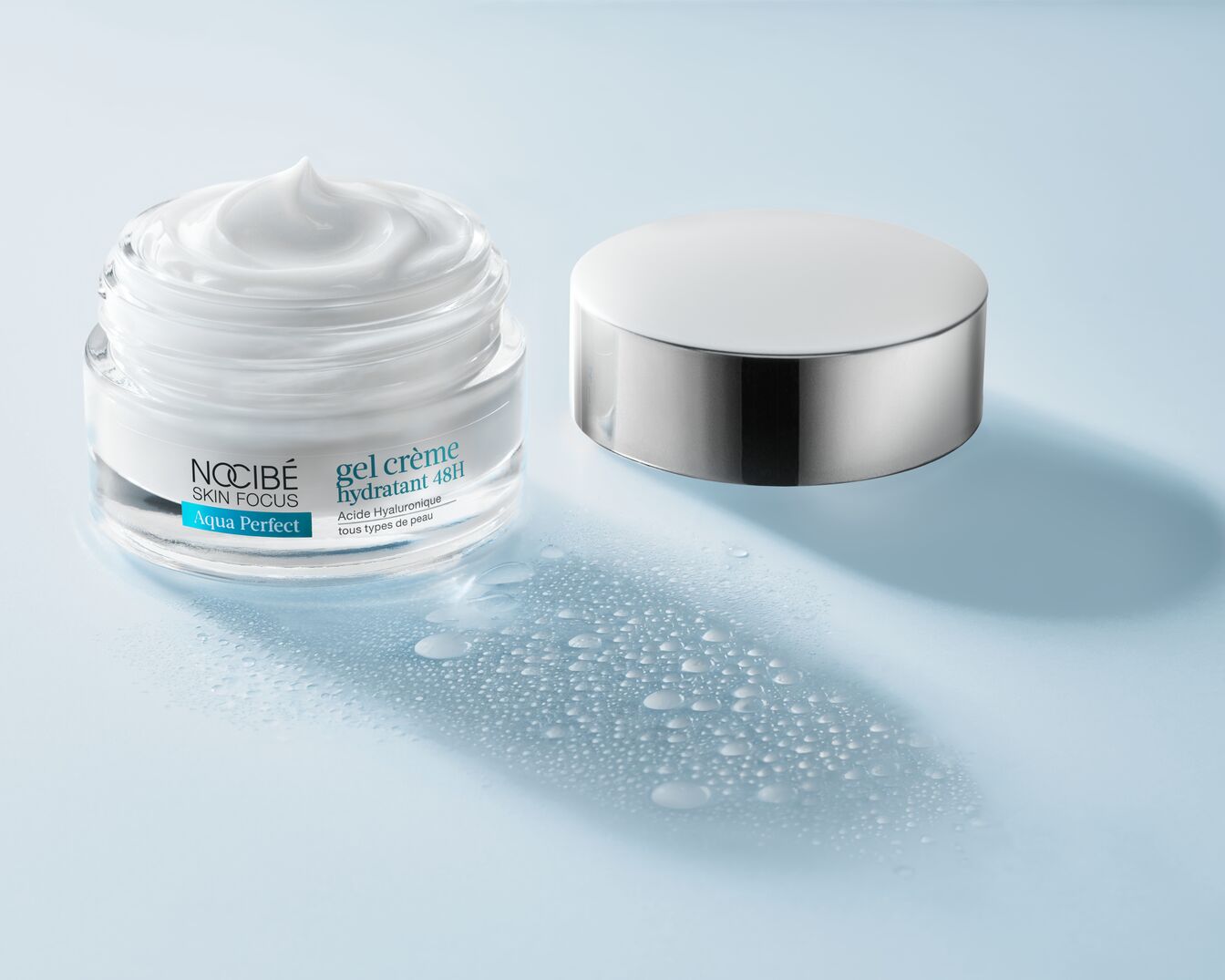 Le gel crème hydratant 48H Nocibé Skin Focus Aqua Perfect à l'acide hyaluronique, présenté dans un pot en verre transparent avec un couvercle argenté, est idéal pour tous les types de peau.
