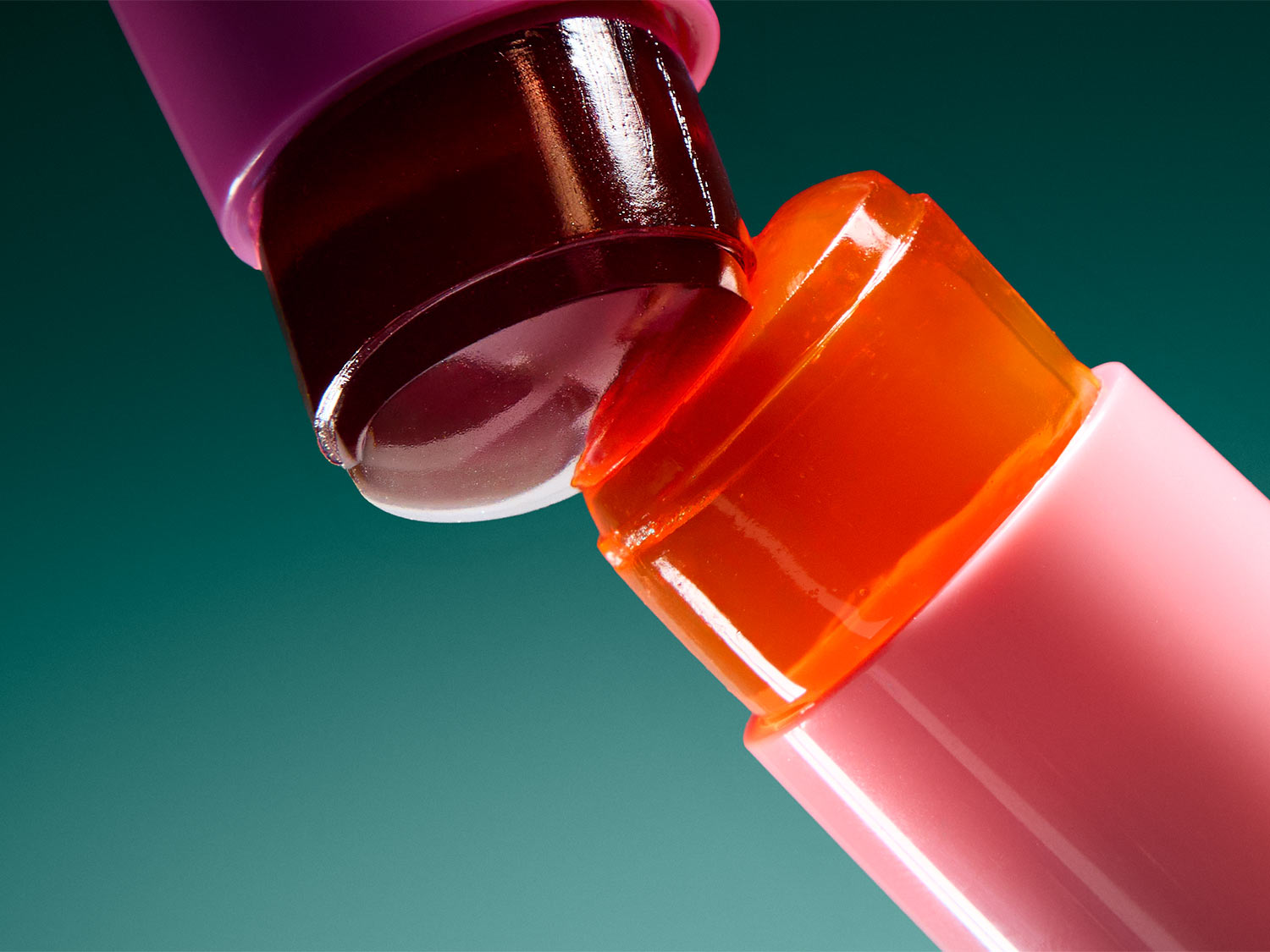 Zwei Lippenstifte, einer in einem dunklen Rotton und der andere in einem leuchtenden Orange, sind schräg zueinander positioniert, wobei sich ihre Spitzen berühren und einen glänzenden, feuchten Effekt erzeugen.