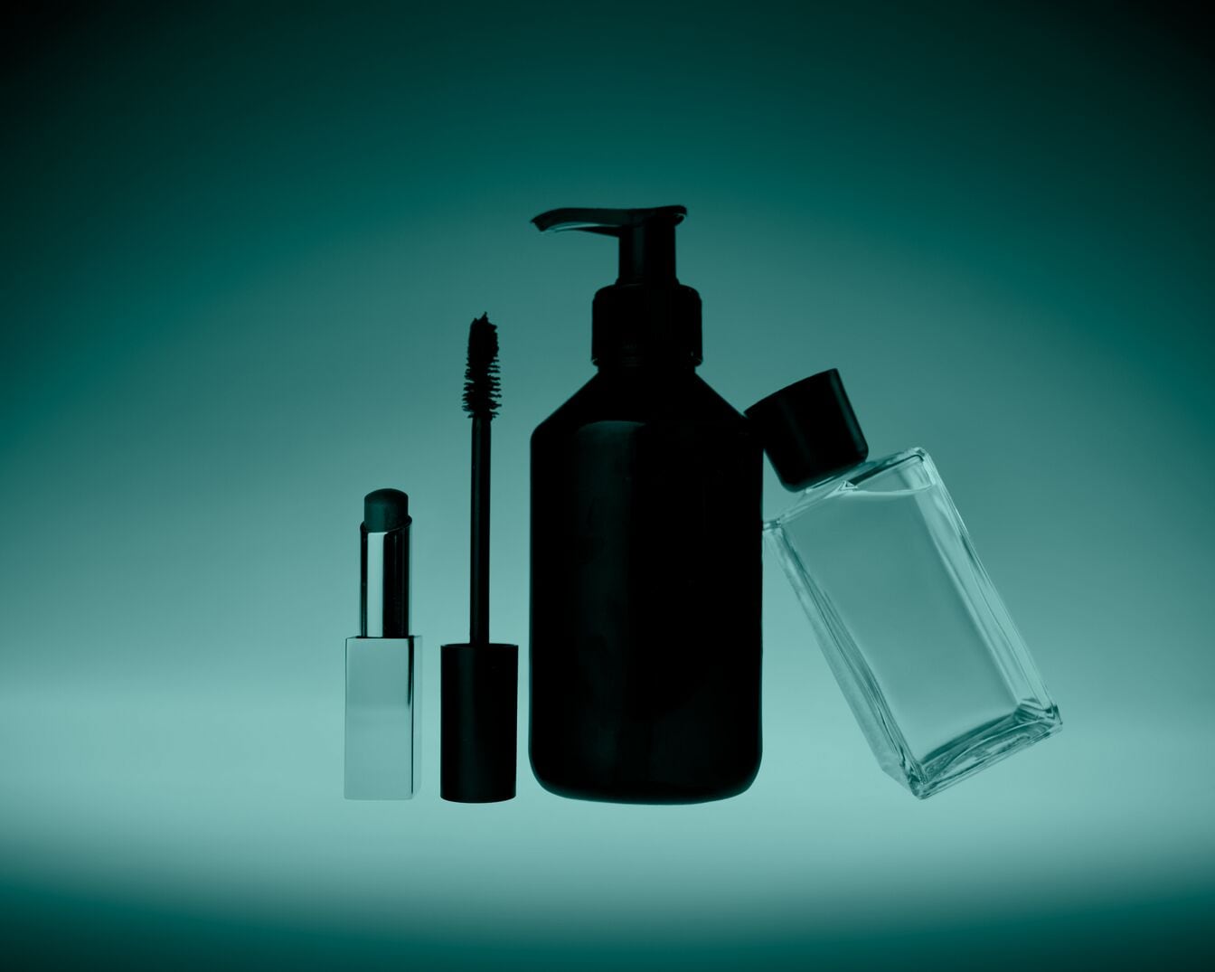 Een stilleven van schoonheidsproducten, waaronder een zilveren lippenstift, een mascara met een borsteltje, een zwarte pompflacon en een heldere glazen parfumfles, allemaal tegen een donkergroene achtergrond.