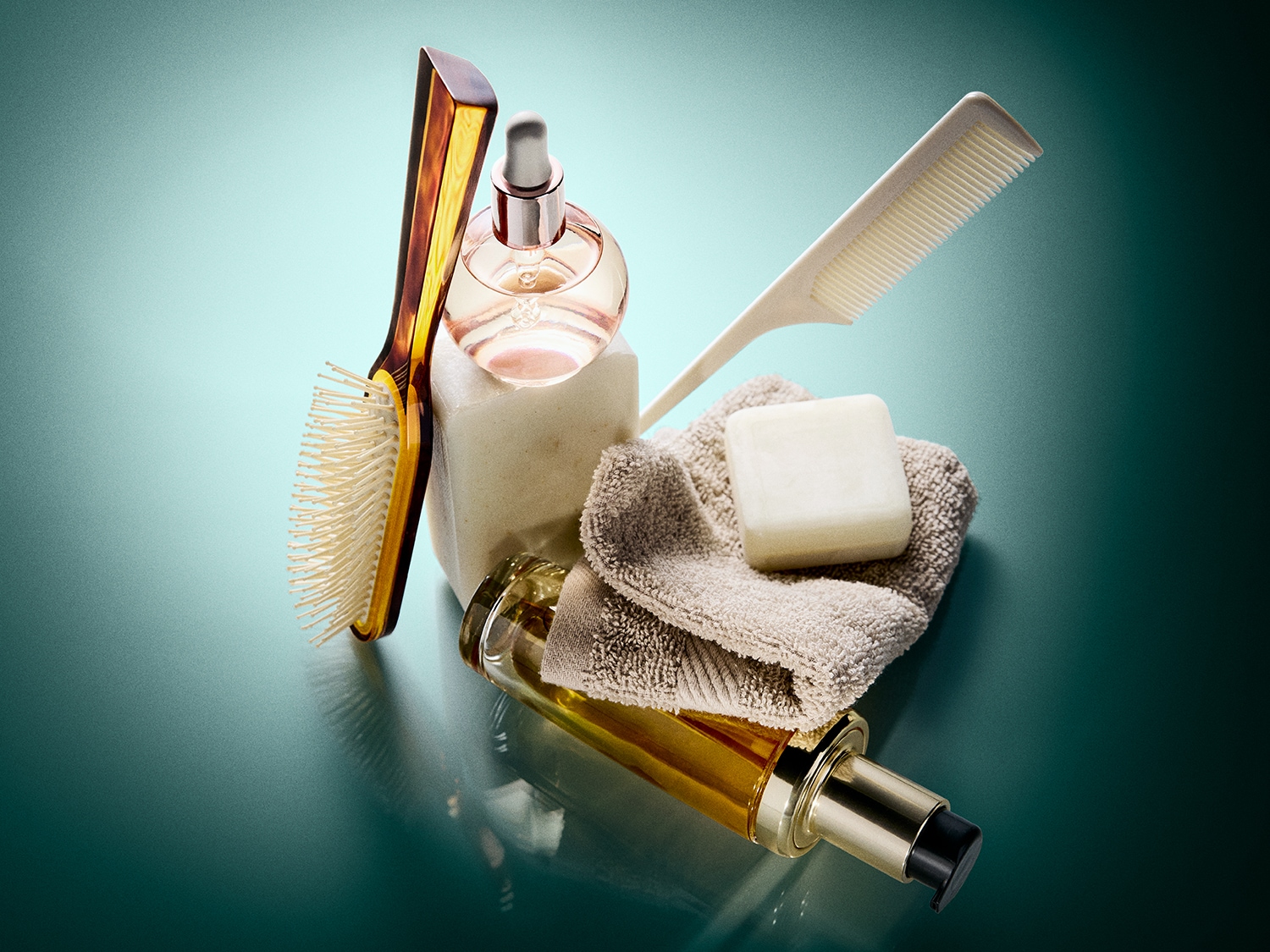 Een verzameling badkamerbenodigdheden, waaronder een borstel met een bruin handvat, een flesje parfum met een pipet, een stuk zeep, een opgerolde handdoek, een kam en een flesje olie met een pompje, allemaal op een glanzend groen oppervlak.
