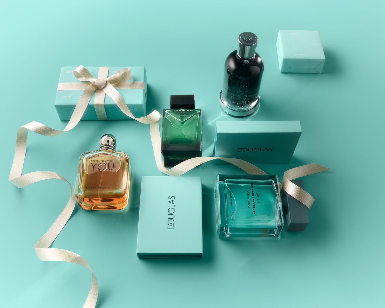 Eine Auswahl an Parfümflaschen und Douglas-Geschenkboxen in Türkis, darunter Emporio Armani Stronger With You, Prada und Narciso Rodriguez, elegant arrangiert mit einem goldenen Band auf türkisfarbenem Hintergrund.