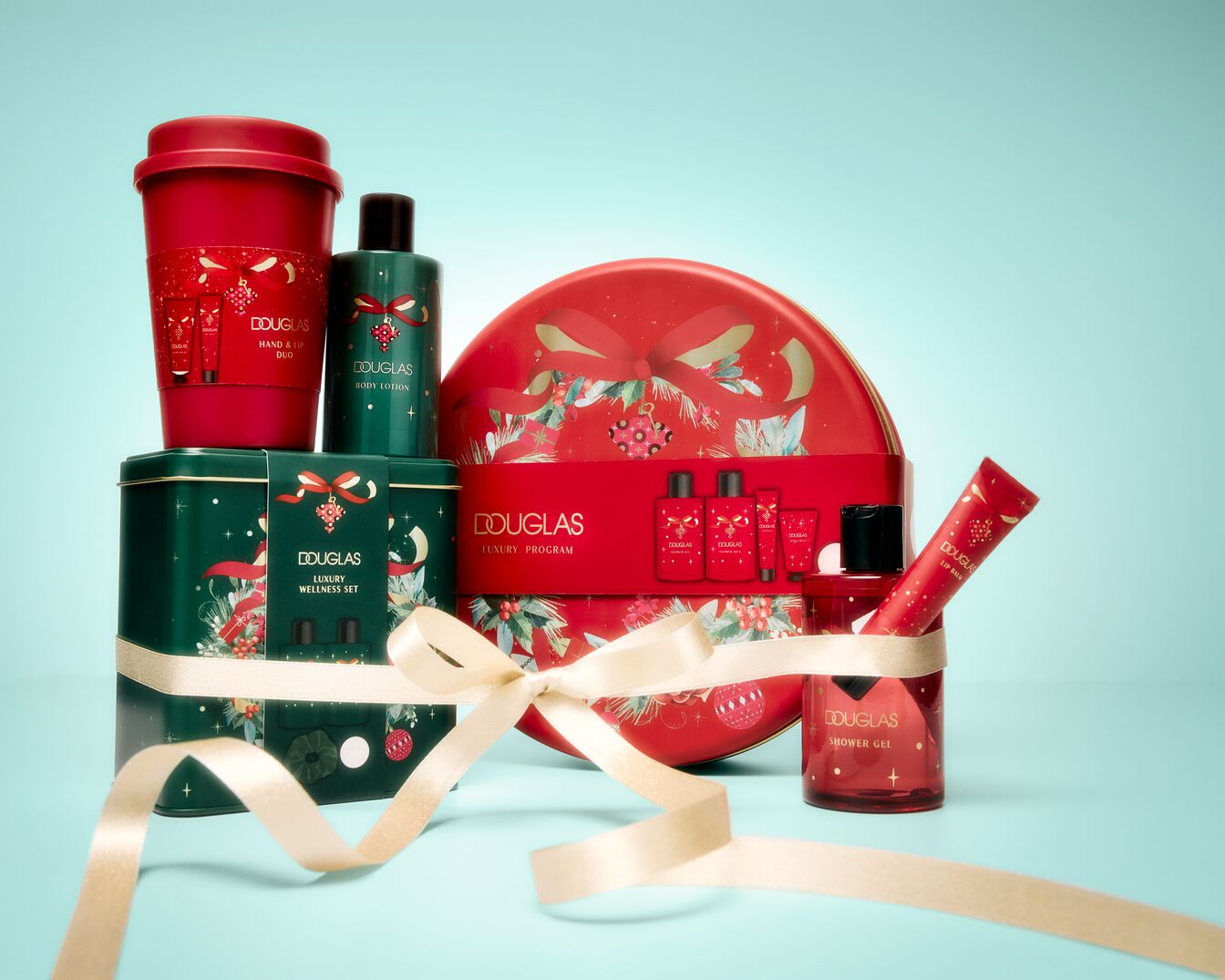 Das Douglas Geschenkset enthält eine rote Tasse mit Hand- und Lippenduo, eine grüne Flasche Body Lotion, eine grüne Wellness-Box, eine rote Dose mit Luxusprogramm-Produkten, ein rotes Duschgel und einen roten Lip Balm, alles mit einem goldenen Band verziert.