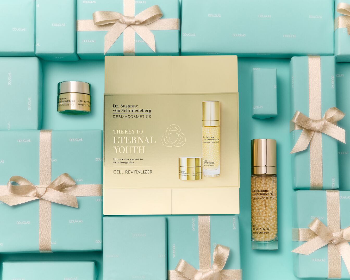 Setul cadou Dr. Susanne von Schmiedeberg CELL REVITALIZER, cu ambalaj auriu și alb, include o cremă de longevitate și un ser lichid, înconjurat de cutii turcoaz cu panglici aurii, perfect pentru a debloca secretul tinereții eterne.