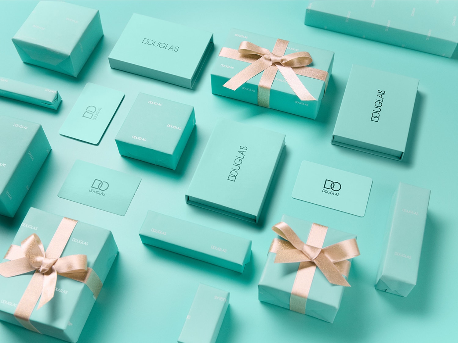 Eine Ansammlung von Douglas-Geschenkboxen und -Karten in Türkis, einige mit goldenen Bändern verziert, liegt auf einem passenden türkisfarbenen Hintergrund.