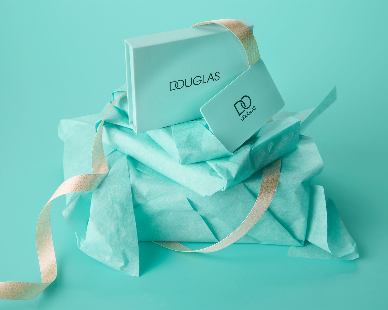 Een Douglas geschenkdoos en cadeaukaart in een zachtgroene kleur, omwikkeld met zijdepapier en een goudkleurig lint, klaar om cadeau te geven.