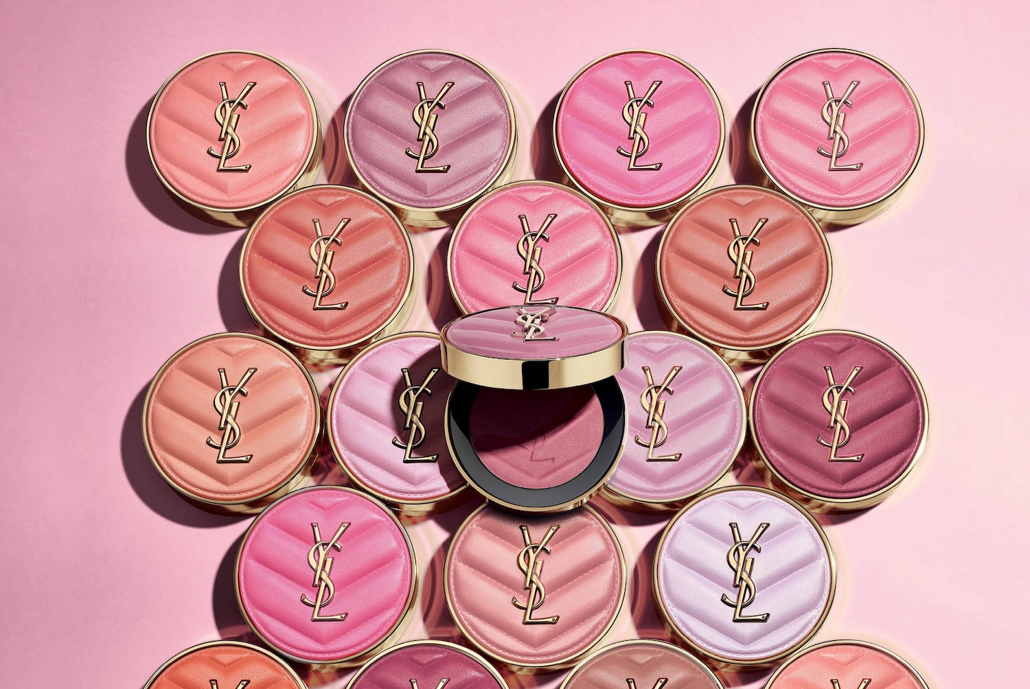 Kompaktowe róże do policzków YSL Couture Blush w różnych odcieniach różu i brązu, z wytłoczonym logo YSL na pikowanym wieczku, ułożone na różowym tle.