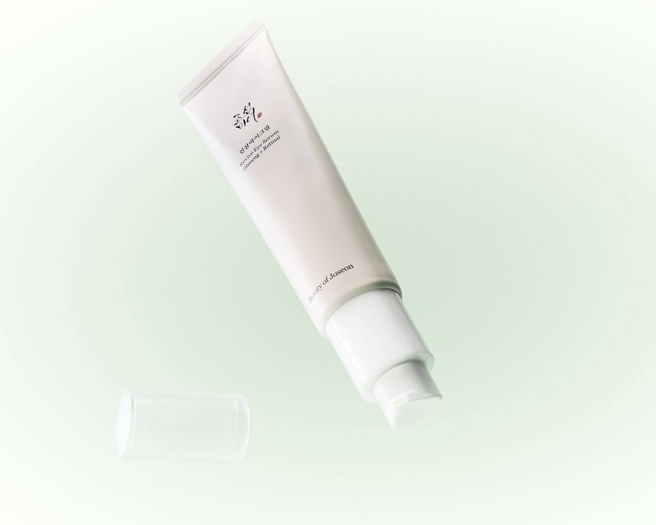 Die Beauty of Joseon Revive Eye Serum Ginseng + Retinal ist eine hellbeige Tube mit einem weißen Pumpspender und einer transparenten Kappe, die auf einem hellgrünen Hintergrund schwebt.