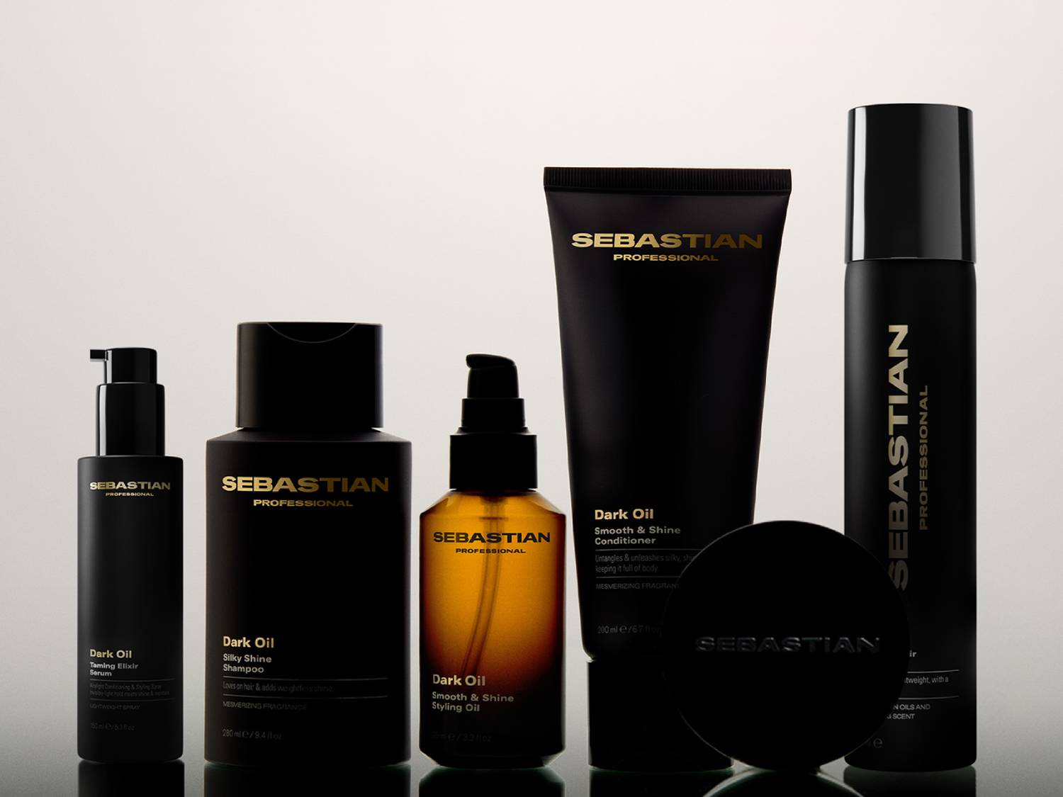 Kolekcja Sebastian Professional Dark Oil to sześć eleganckich, czarnych butelek i słoików z pompkami i zakrętkami, zawierających szampon, odżywkę, serum, olejek do stylizacji i inne produkty do włosów, wszystkie z etykietami w kolorze złotym.