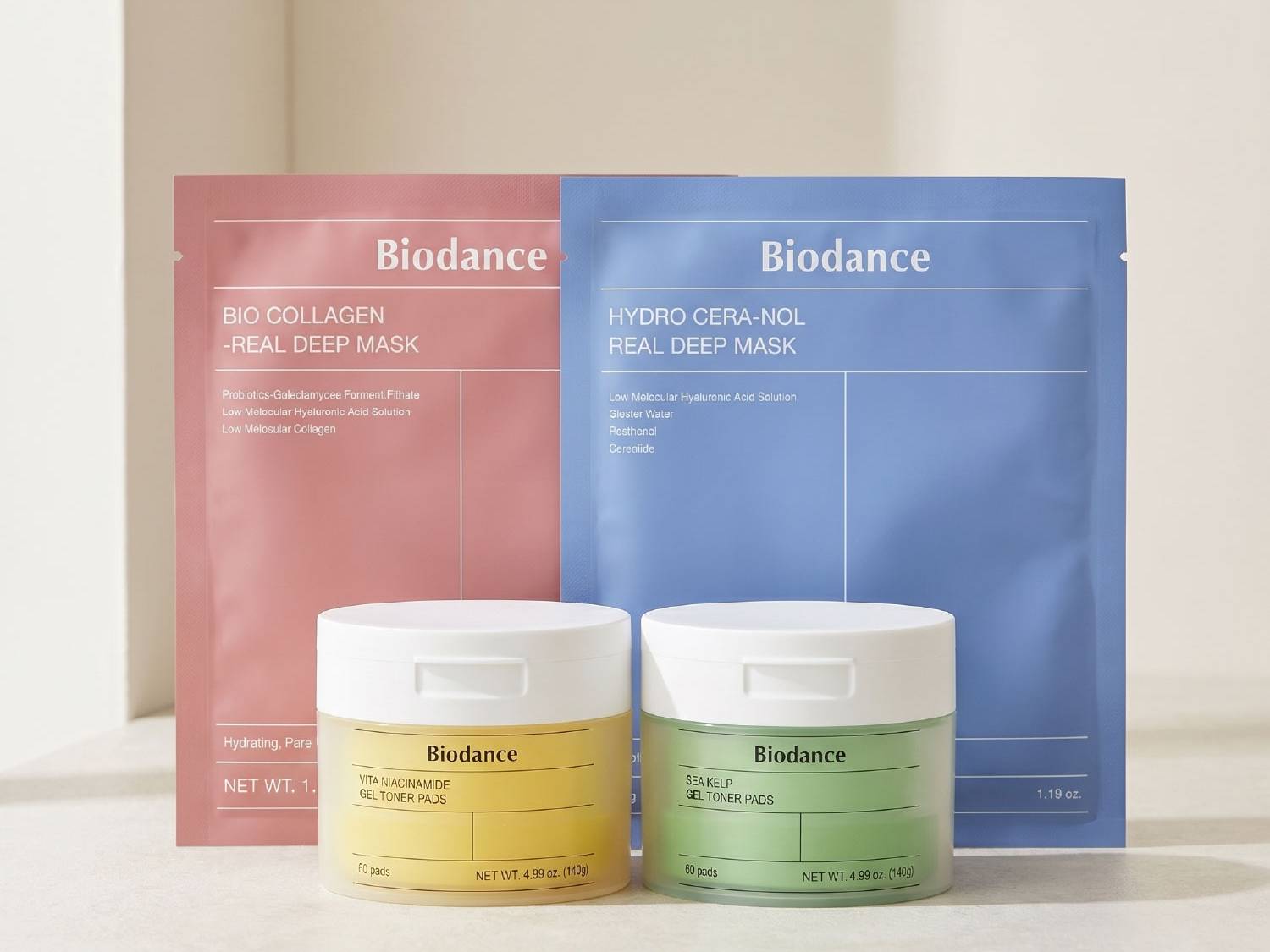 Dwie maski Biodance Bio Collagen Real Deep Mask w różowym opakowaniu i Hydro Cera-Nol Real Deep Mask w niebieskim opakowaniu, obok nich dwa słoiczki z żelowymi płatkami tonizującymi Vita Niacinamide w żółtym i Sea Kelp w zielonym kolorze, wszystkie produkty są gotowe do użycia.