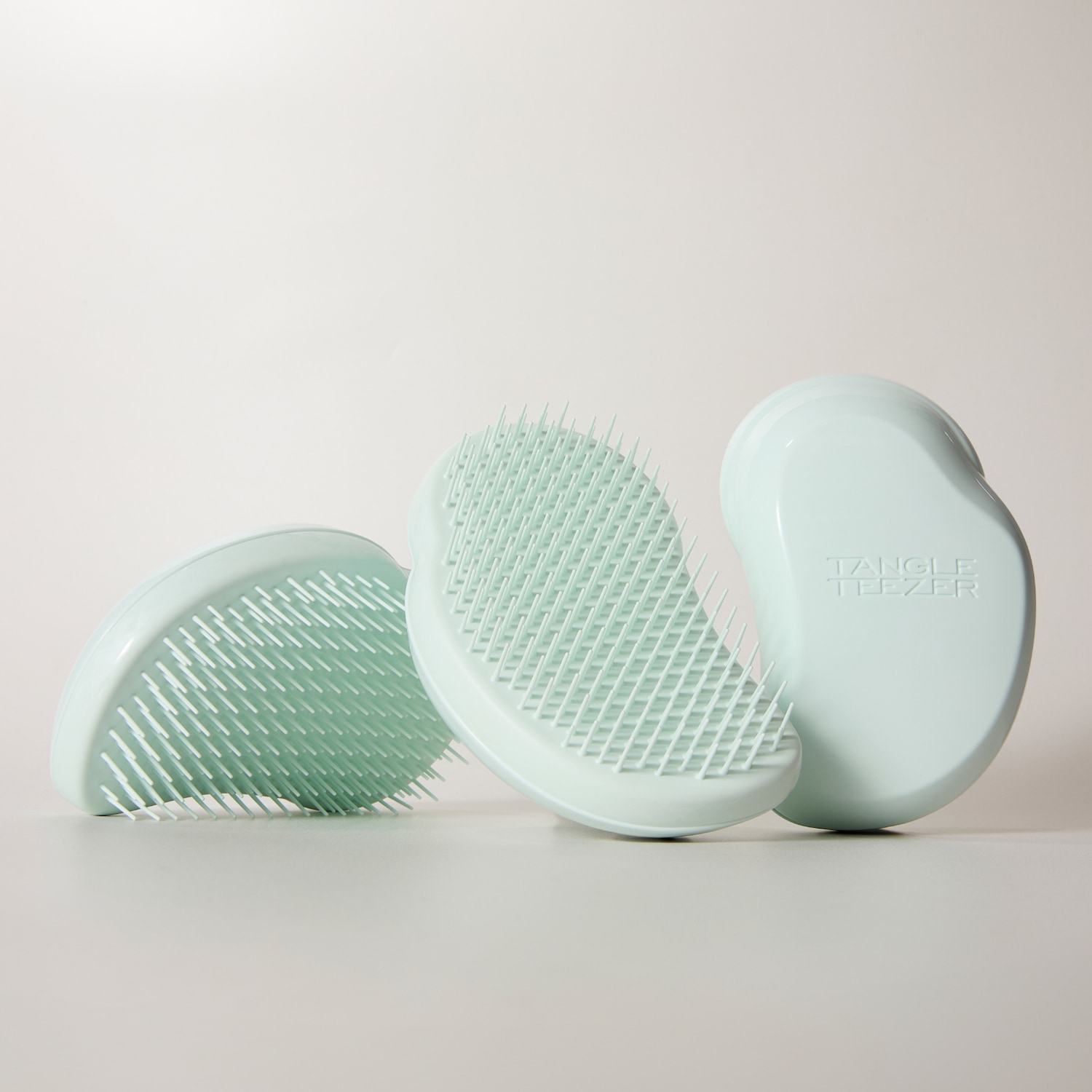 Drei hellblaue Tangle Teezer Haarbürsten sind auf einem hellen Hintergrund angeordnet, wobei zwei Bürsten mit den Borsten nach oben und eine mit der Rückseite nach vorne positioniert sind, auf der das Tangle Teezer Logo zu sehen ist.