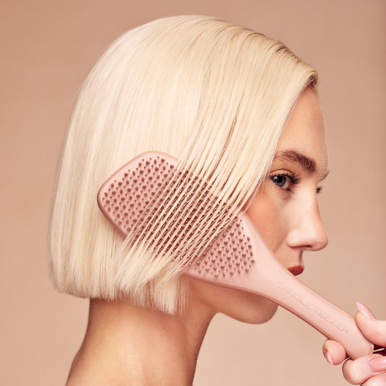 Eine Frau mit kurzem, blondem Haar kämmt sich mit einer rosafarbenen Tangle Teezer Bürste, die sanft durch ihr Haar gleitet und es entwirrt.