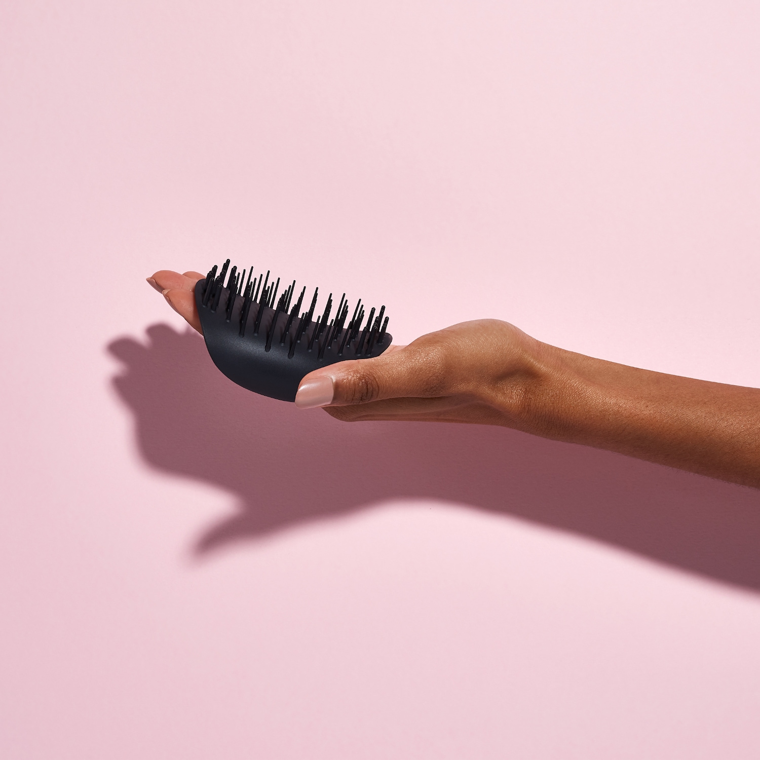 Eine Hand hält eine schwarze Kopfhautbürste mit weichen Borsten, die sanft die Kopfhaut massieren und peelen, um die Durchblutung zu fördern und das Haarwachstum anzuregen.