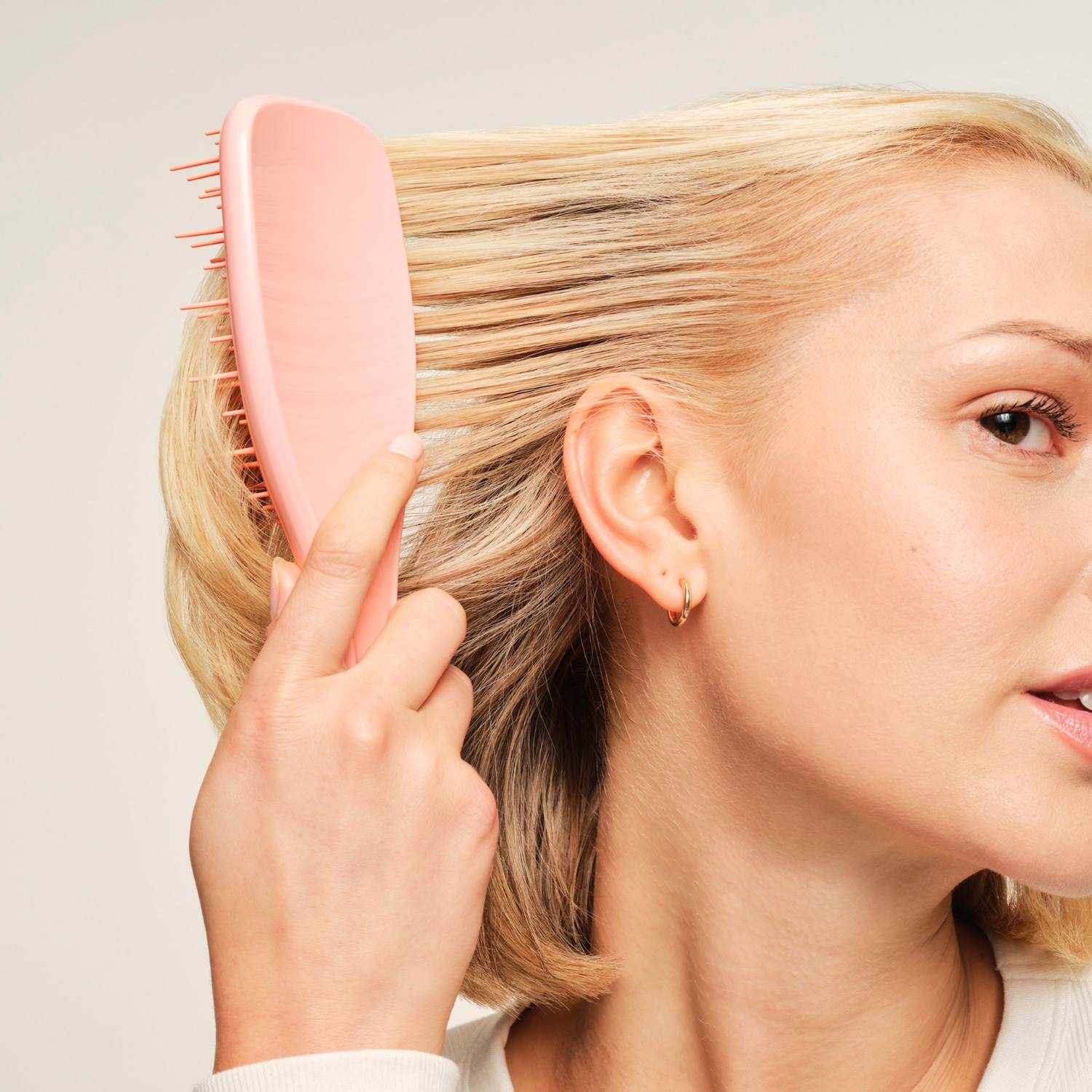 Eine Frau kämmt ihr blondes Haar mit einer rosafarbenen Bürste, die sanft durch die Strähnen gleitet und für ein glattes, entwirrtes Ergebnis sorgt.
