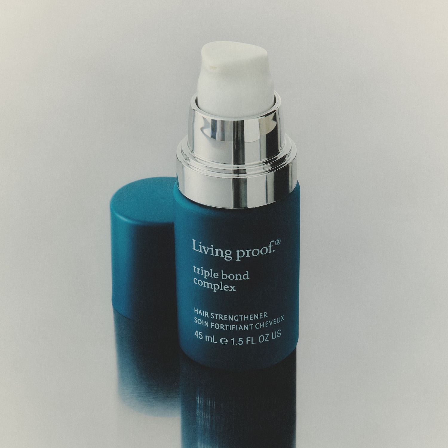 Living Proof Triple Bond Complex Haarstärker in einer 45 ml blauen Flasche mit silbernem Spender und weißem Pumpkopf, daneben liegt der blaue Deckel.