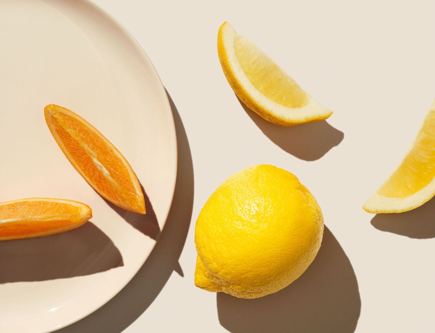 Une assiette beige est placée sur une surface claire, avec deux quartiers d'orange et un citron entier, ainsi que deux quartiers de citron, créant une composition fraîche et lumineuse.