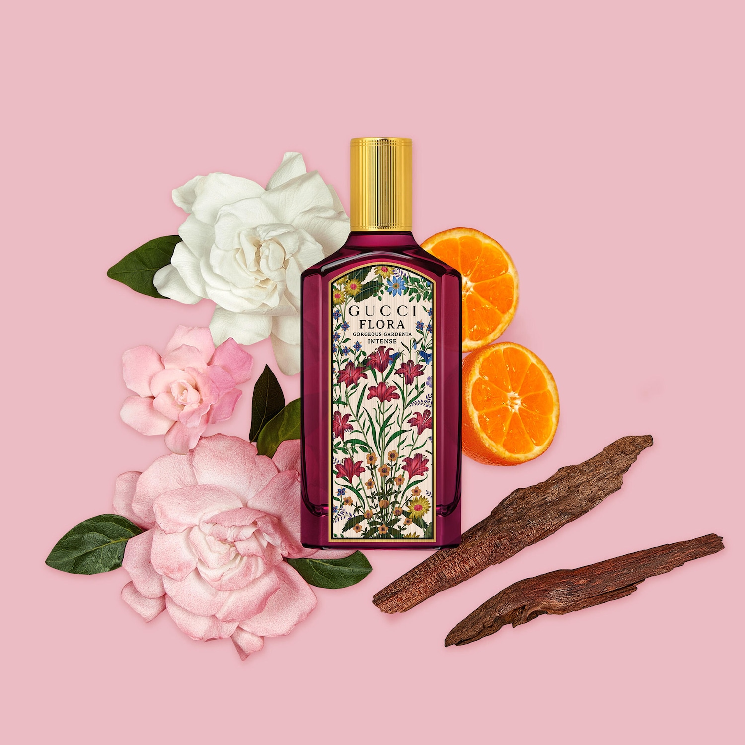 Parfém Gucci Flora Gorgeous Gardenia Intense v tmavě růžovém flakonu se zlatým uzávěrem, zdobený květinovým vzorem, je obklopen bílými a růžovými květy gardénie, plátky pomeranče a kousky dřeva na růžovém pozadí.