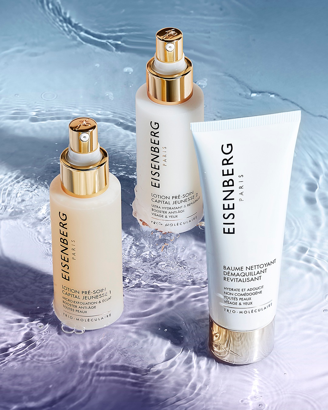 Tres productos Eisenberg Paris, que incluyen dos lociones pre-tratamiento y un bálsamo limpiador revitalizante, se muestran sobre una superficie de agua con suaves ondas.