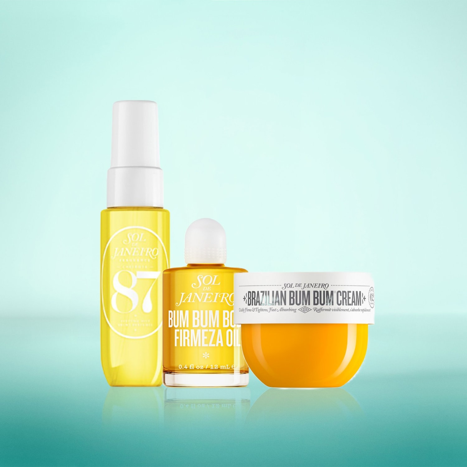 Das Bild zeigt drei Sol de Janeiro Produkte: ein gelbes Spray mit der Aufschrift "SOL JANEIRO 87", ein kleines gelbes Fläschchen "BUM BUM FIRMEZA OIL" und einen gelben Tiegel "BRAZILIAN BUM BUM CREAM" mit der Aufschrift "Visibly Firms & Tightens, Fast Absorbing".