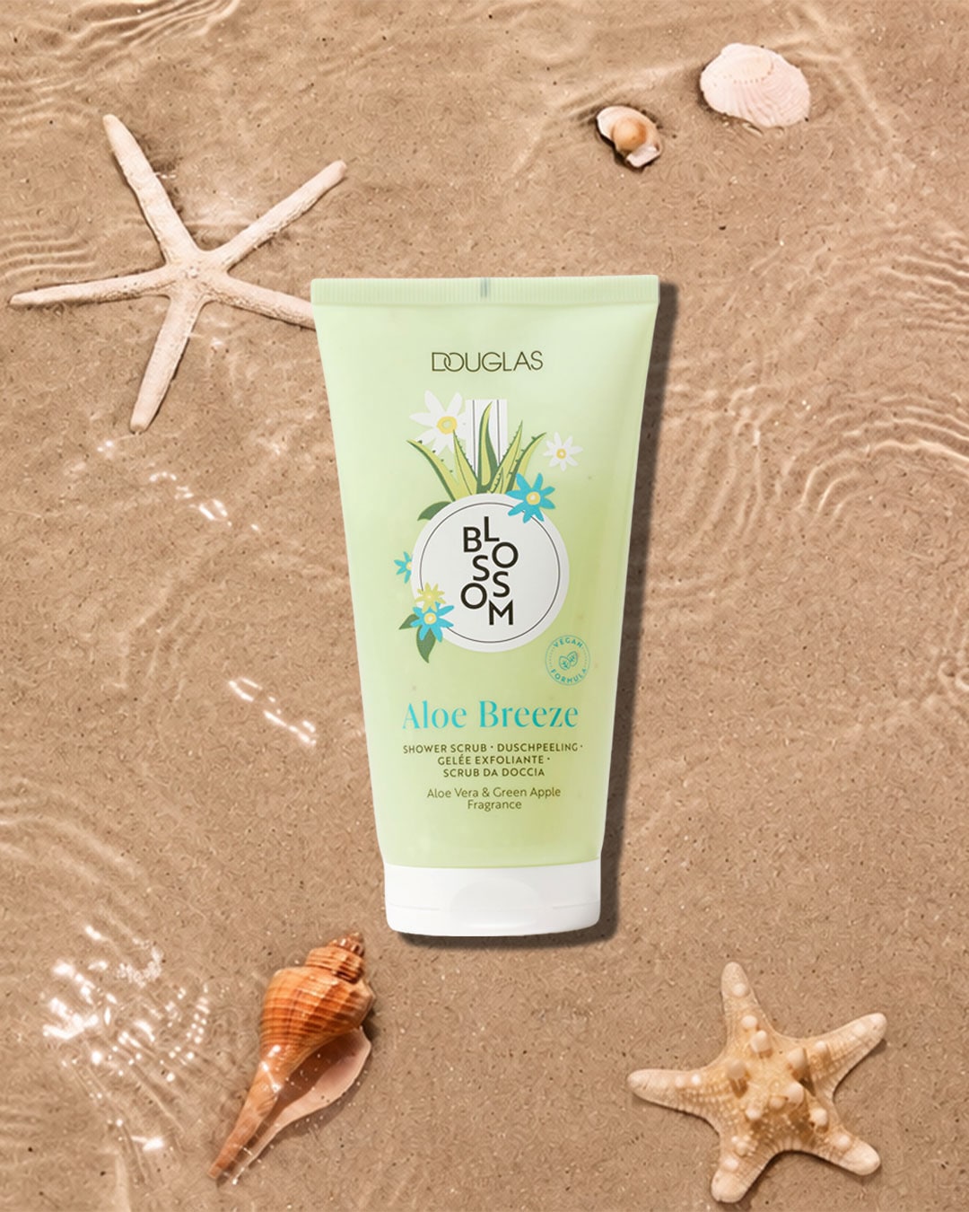 Die Douglas Blossom Aloe Breeze Duschpeeling-Tube in Hellgrün mit weißem Deckel liegt auf nassem Sand, umgeben von Seesternen und Muscheln, und bietet einen erfrischenden Duft von Aloe Vera und grünem Apfel.