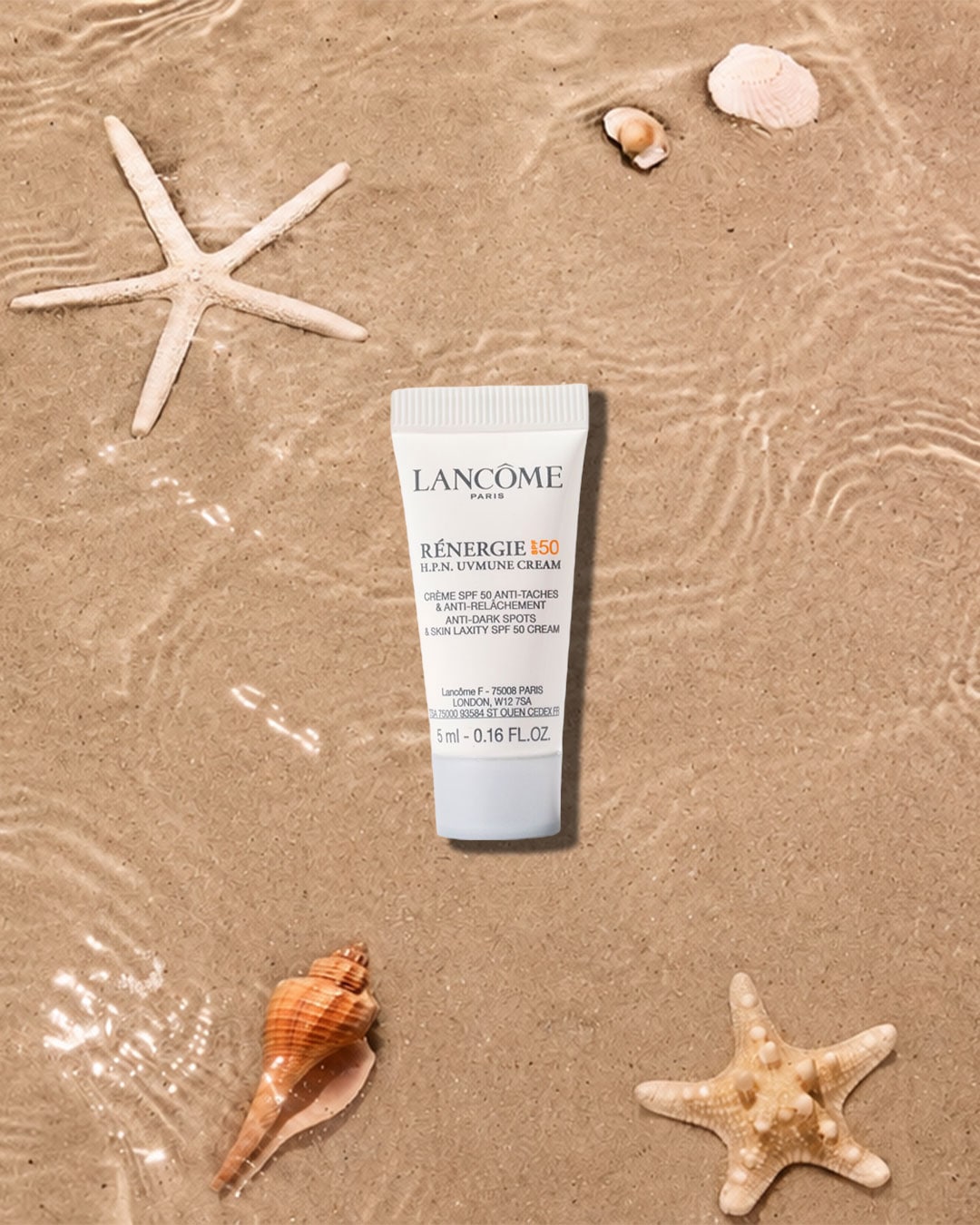 Die Lancôme Rénergie H.P.N. UVMUNE Cream SPF 50, eine weiße Tube mit schwarzer und orangefarbener Schrift, liegt auf nassem Sand, umgeben von Seesternen und Muscheln.